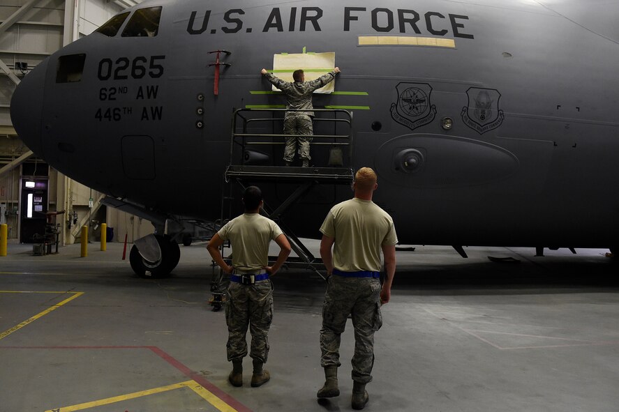 Airmen from the 62nd Maintenance Squadron apply a stencil to a 62nd Airlift Wing C-17 Globemaster III for the naming of the aircraft May 12, 2016 at Joint Base Lewis-McChord, Wash.” The name, “Flying the Hump” comes from the airlift missions, known as flying the hump, that were flown over the Himalayan Mountains between India and China from 1943 to 1945 involving U.S. C-46 Commandos and C-47 Skytrains. As it is extremely rare for a C-17 to be named, this marks the 4th aircraft out of 48 assigned C-17s at McChord Filed to receive this honor. (U.S. Air Force photo/Tech. Sgt. Tim Chacon) 