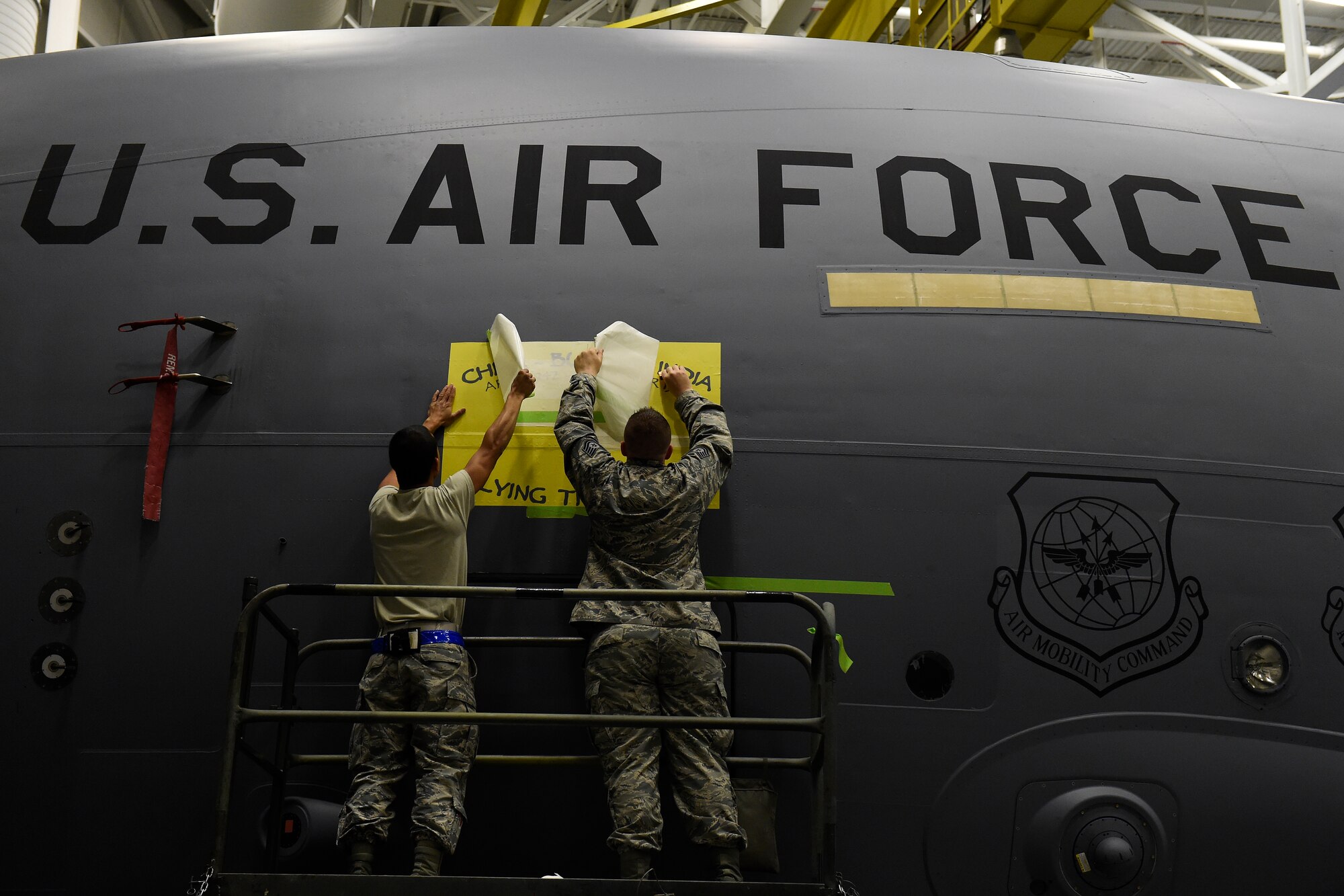 Staff Sgt. Ben Dominquez (left) and SrA Brandon Breshears, 62nd Maintenance Squadron structural maintenance mechanics, apply a stencil to a 62nd Airlift Wing C-17 Globemaster III for the naming of the aircraft May 12, 2016 at Joint Base Lewis-McChord, Wash. The name, “The Spirit of the Hump” comes from the airlift missions, known as flying the hump, that were flown over the Himalayan Mountains between India and China from 1943 to 1945 involving U.S. C-46 Commandos and C-47 Skytrains. (U.S. Air Force photo/Tech. Sgt. Tim Chacon) 