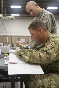 CAMP ATTERBURY, Ind. -- Staff Sgt. John Webb, night shift battle staff member during training exercise Vibrant Response 16, looks up information for Capt. James Saccheti, Task Force 76 night shift battle captain. Webb is with the 385th Military Battalion in Fort Stewart, Ga.; while Saccheti is of the 302d Maneuver Enhancement Brigade based in Chicopee, Mass. (U.S. Army photo by Sgt. Anshu Pandeya)