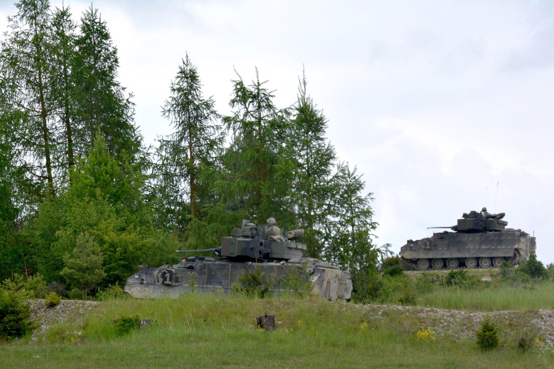 Two M2A3 Bradley fighting vehicles bound over the terrain during a platoon’s Gunnery Table XII at Grafenwoehr Training Area, Germany, May 19, 2016. Army photo by Maj. Randy Ready