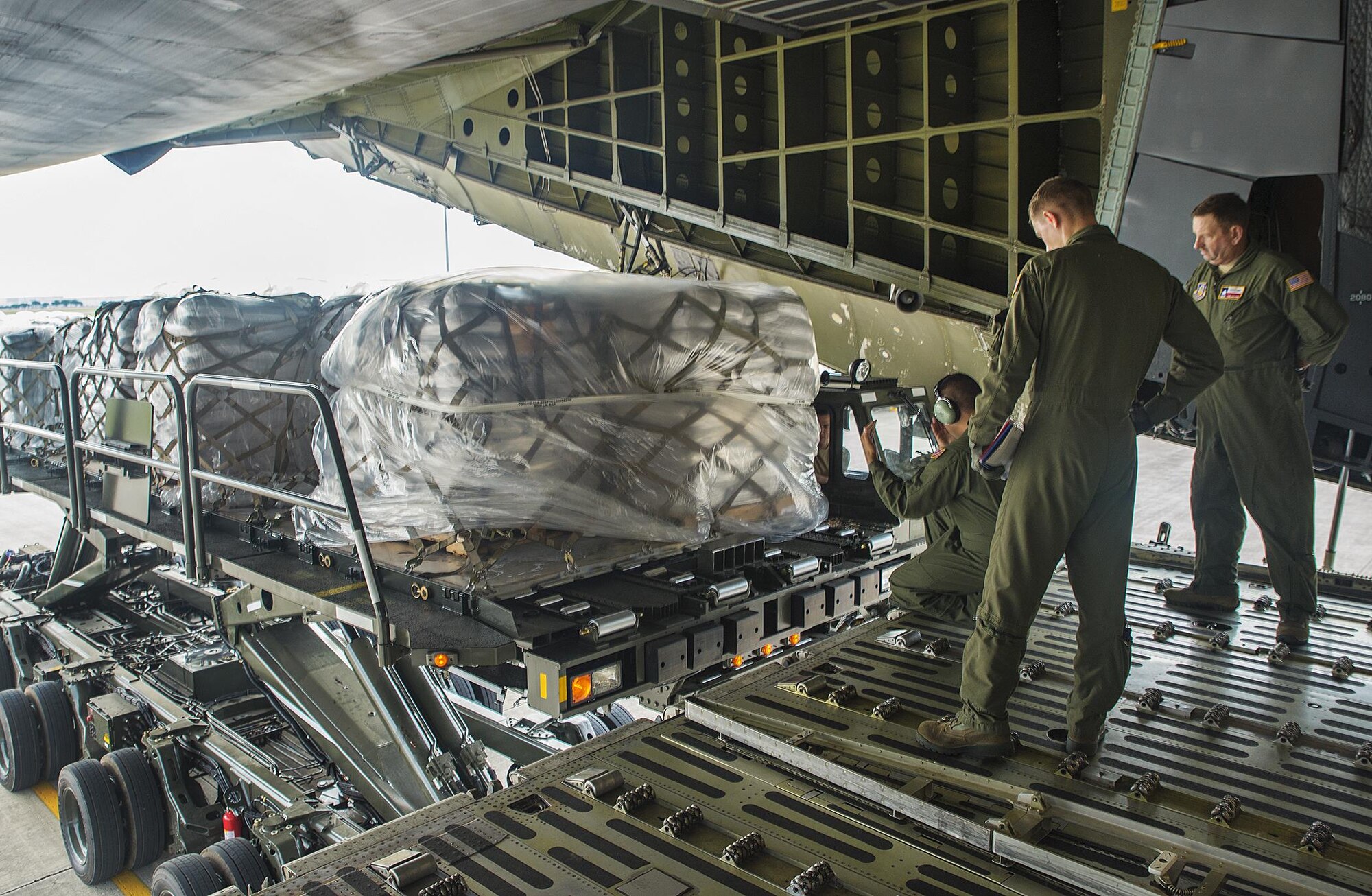 Airmen with the 356th Airlift Squadron direct an Atlas K-loader to an awaiting C-5M Super Galaxy aircraft May 13, 2016 at Joint Base San Antonio-Lackland, Texas. The 433rd Airlift Wing and 502nd Logistics Readiness Squadron worked together to ensure 90,000 pounds of food aid made it to Yoro, Honduras. (U.S. Air Force photo by Benjamin Faske) 