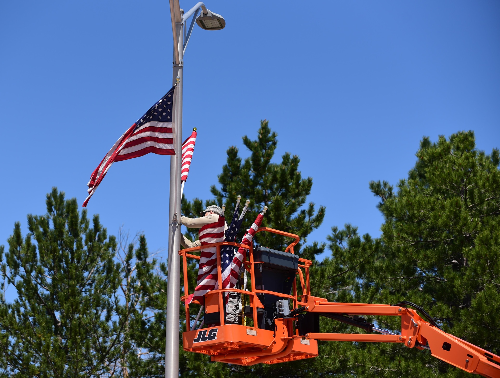 Staff Sgt. Steven Price, 21st Civil Engineer Squadron structural journeyman, attaches American flags to the light poles running down Stewart Avenue for Memorial Day at Peterson Air Force Base, Colo., May 23, 2016.  Part of a two-man team, Price was responsible for placing around 130 flags along the main roads of the base to commemorate the holiday weekend. (U.S. Air Force photo by Staff Sgt. Amber Grimm)
