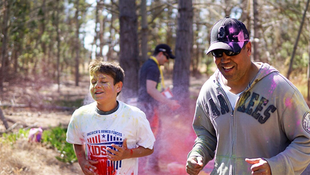 Master Sgt. Enrique Santiago, 30th Space Wing wing 3A functional manager, and his son Elijah Santiago, run through colored cornstarch haze during the “Kids Color Run” hosted by the Youth Center, May 21, 2016, Vandenberg Air Force Base, Calif. The run has been a recurring event on Vandenberg since 2002, always taking place on Armed Forces Day, although it wasn’t until a few years ago that colored powder was added which increased participation.