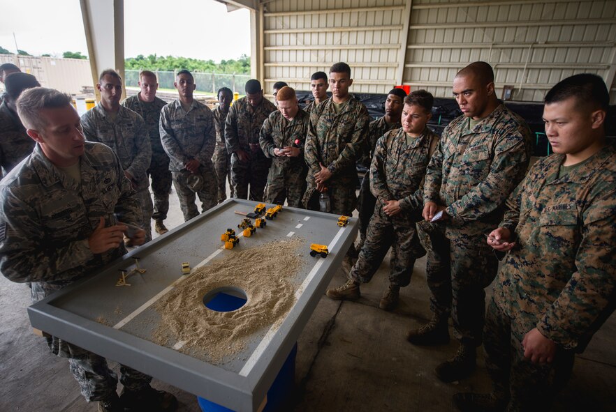 Airmen and Marines gather around a display model to go over the joint airfield damage repair exercise May 19, 2016 at Kadena Air Base, Japan. During the exercise, both services learned from each other and improved the operations between each of the services involved. (U.S. Air Force photo by Senior Airman Omari Bernard)
