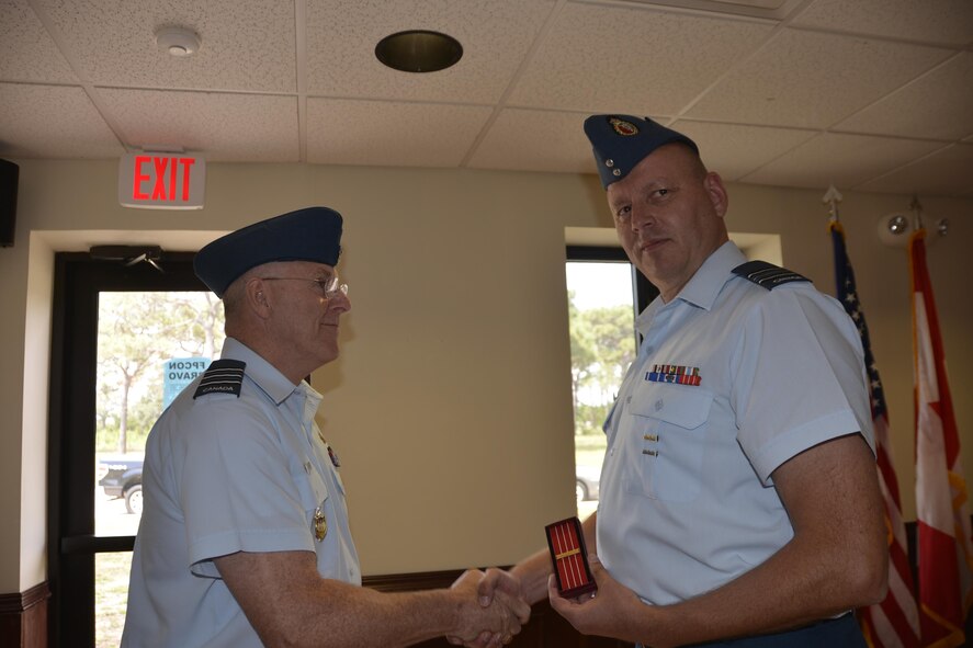 Royal Canadian Air Forces LCol Larry Weir, outgoing Canadian Detachment Commander, congratulates Royal Canadian Air Forces Maj David Kruger, Continental U.S. Aerospace Defense Region-1st Air Force (Air Forces Northern) Intelligence Directorate, after presenting him with the Canadian Forces’ Decoration Clasp, prior to the Canadian Detachment Change of Command Ceremony May 18. The decoration is awarded to members of the Canadian Forces of all ranks who have completed 12 years of service with a record of good conduct. A clasp is awarded for every subsequent 10 years designated by a silver rosette. (Air Force Photo released/Mary McHale)