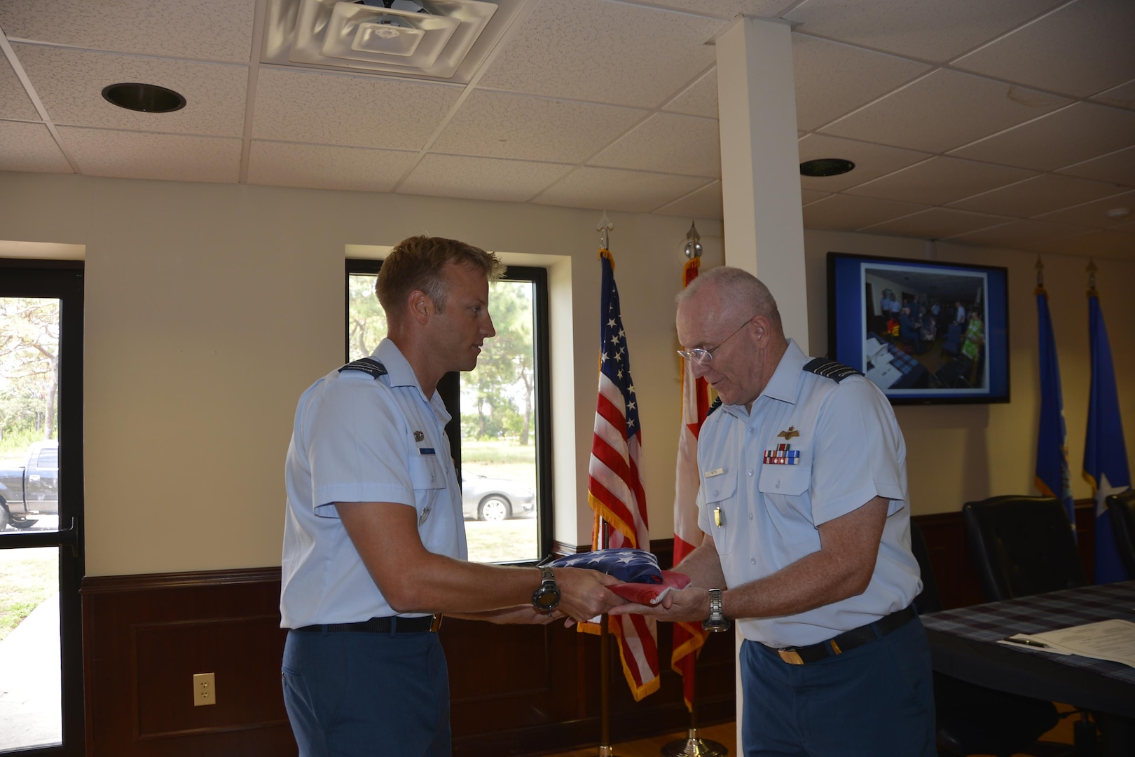 Royal Canadian Air Force Maj Reid Surkan, Continental U.S. Aerospace Defense Region-1st Air Force (Air Forces Northern) Plans, Policy and International Military Affairs Directorate, presents folded Canadian and American flags to LCol Larry Weir, in recognition of Weir’s honorable tenure as Canadian Detachment Commander during a change of command ceremony here May 18. During the ceremony, Weir relinquished command to LCol Brian Murray. (Air Force Photo released/Mary McHale)