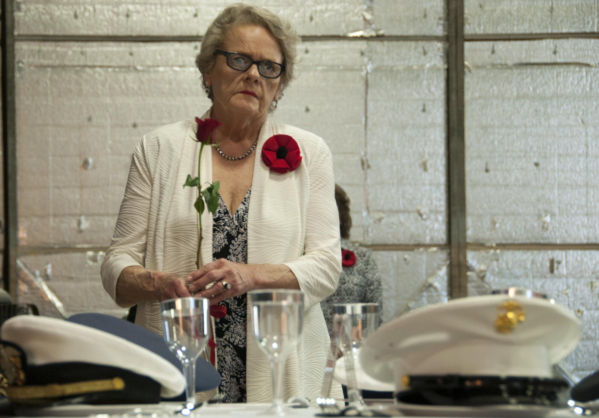 A member of the American Legion Auxillary 626 approaches a table set for those who never came home from war with a red rose, during the Vietnam War Veterans Recognition Ceremony at Naval Air Station Fort Worth Joint Reserve Base, Texas, April 22. The flower serves as a reminder of service members who are or were missing and those who are still waiting and seeking answers. (U.S. Air Force photo by Staff Sgt. Melissa Harvey)