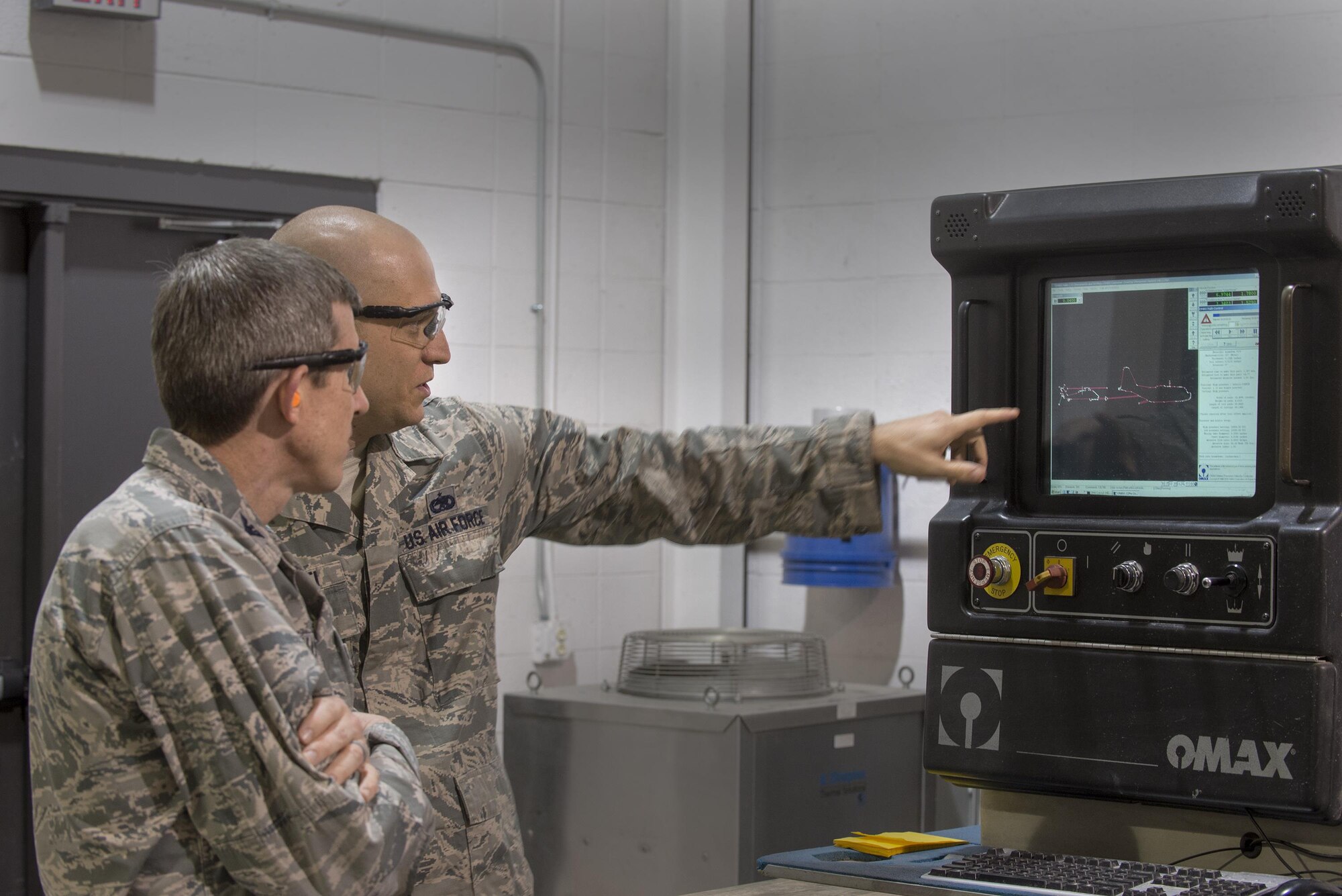 U.S. Air Force Staff Sgt. Ian Marietti, 23d Equipment Maintenance Squadron aircraft metals technology craftsman, right, explains the water jet machining center to Col. Thomas Kunkel, 23d Wing commander, Jan. 25, 2016, at Moody Air Force Base, Ga. The machine has the ability to cut through up to six inches of steel at two and half times the speed of sound. (U.S. Air Force photo by Airman Daniel Snider/Released)