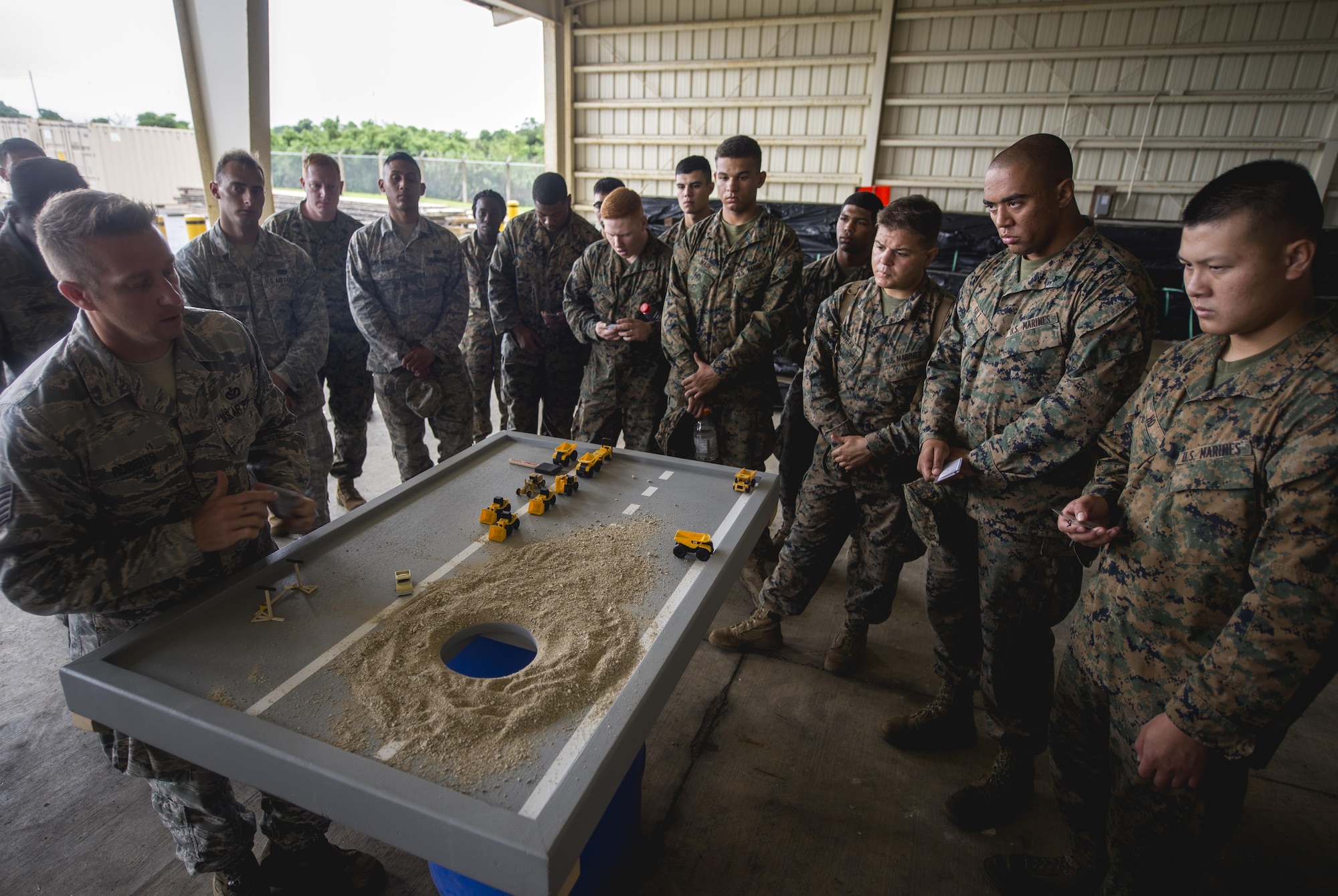 Airmen and Marines gather around a display model to go over a joint airfield damage repair exercise May 19, 2016, at Kadena Air Base, Japan. Airmen from the 18th Civil Engineer Squadron taught Marines and Navy Seabees how they repair damaged airfields. (U.S. Air Force photo/Senior Airman Omari Bernard)
