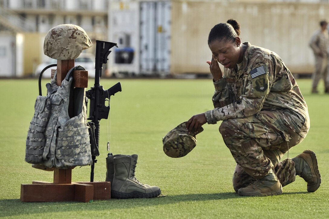 Air Force Master Sgt. Tiffany Robinson kneels in front of a battlefield cross following a Memorial Day ceremony at Camp Lemonnier, Djibouti, May 26, 2014. Robinson is assigned to 449th Air Expeditionary Group. The cross was created with combat gear representing each of the five U.S. military branches to commemorate fallen service members. Navy photo by Petty Officer 1st Class Eric Dietrich