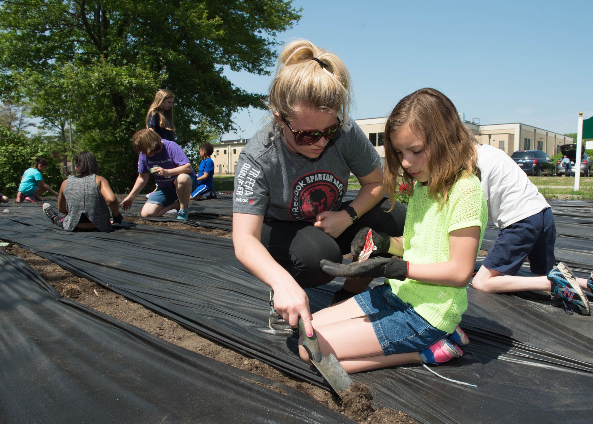 Jillian Wilbur, 66th Force Support Squadron Youth Center clerk, works alongside Sophia Pages planting flowers, herbs and vegetables in the community garden near the Youth Center May 25. Children from the Youth Center were joined by volunteers to plant the community garden for children to enjoy this summer. (U.S. Air Force photo by Jerry Saslav) 