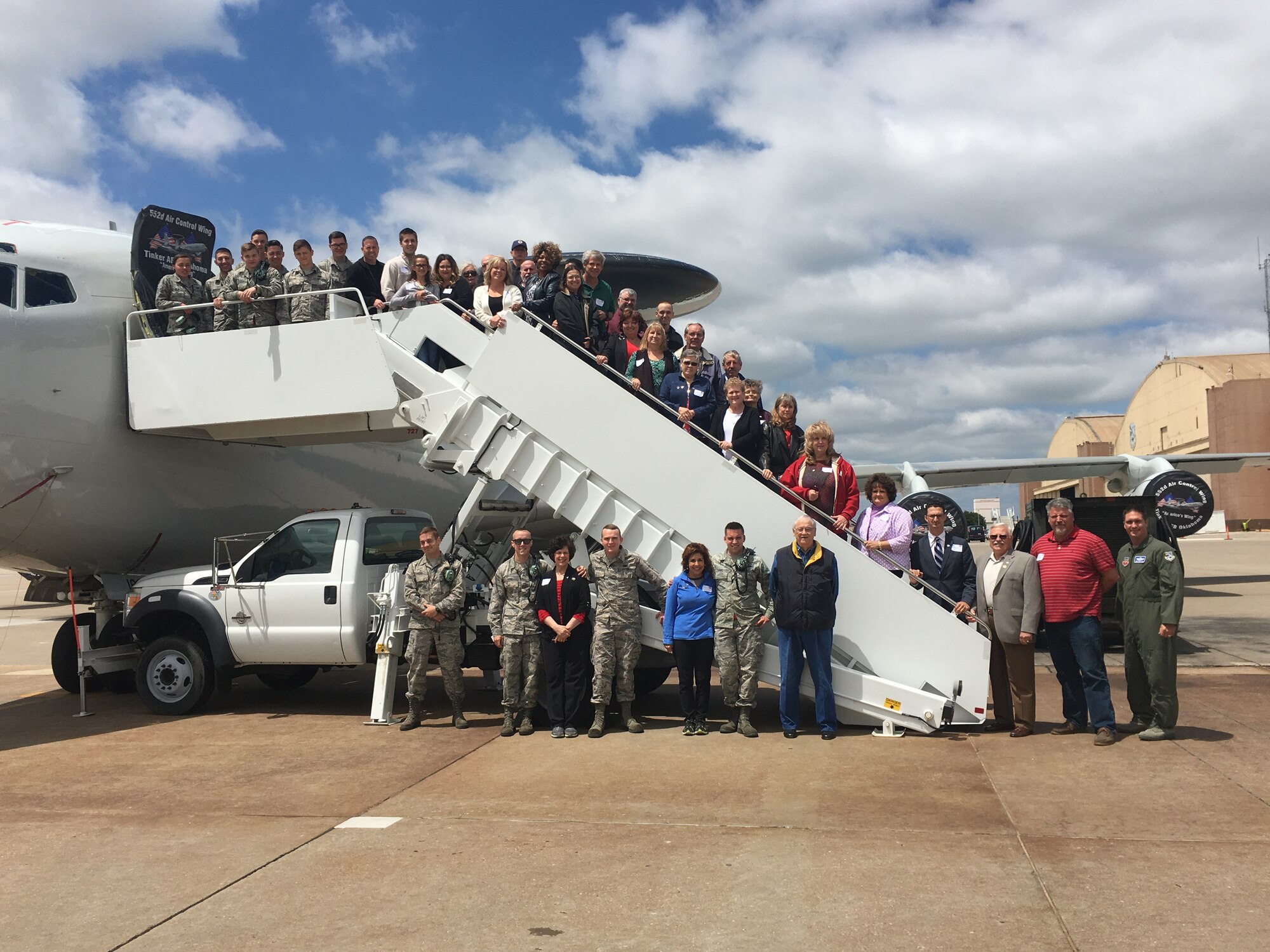 Approximately 30 members of the Home Away from Home program pose for a photograph outside an E-3 “Sentry” Airborne Warning and Control System aircraft as part of a “Team Tinker” tour May 18. The Home Away from Home members represent families who are paired with a Sailor or Airman assigned to Tinker Air Force Base as part of the program to provide them with a place to go and spend time away from work while stationed at Tinker. During their visit to the base, the host community members had lunch at the enlisted dining facility, toured the enlisted dormitories, received unclassified mission briefings from the 552nd Air Control Wing and Navy Strategic Communications Wing ONE and toured an E-3 and Navy E-6B “Mercury” aircraft. (Air Force photo by Michael Della Vecchio/Released)