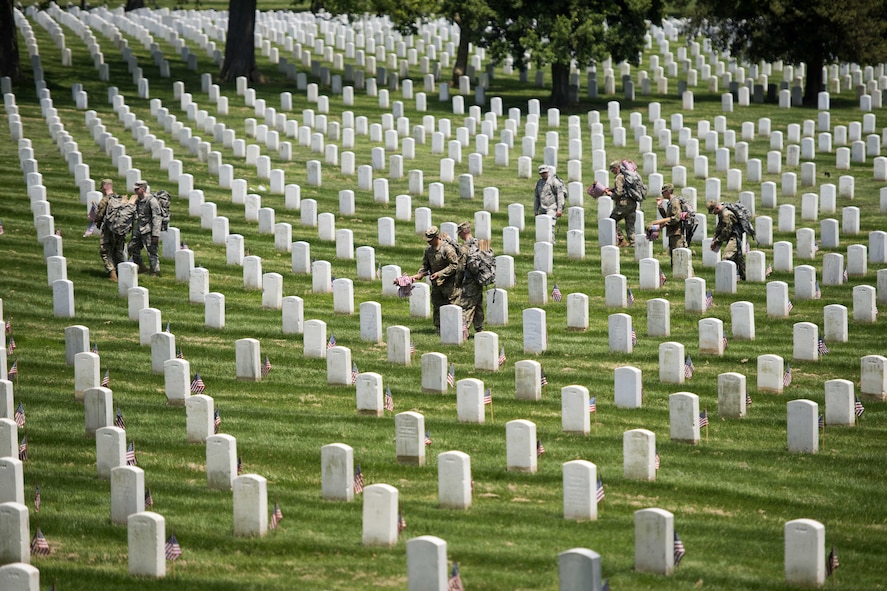 Soldiers placing American flags in front of headstones during 
