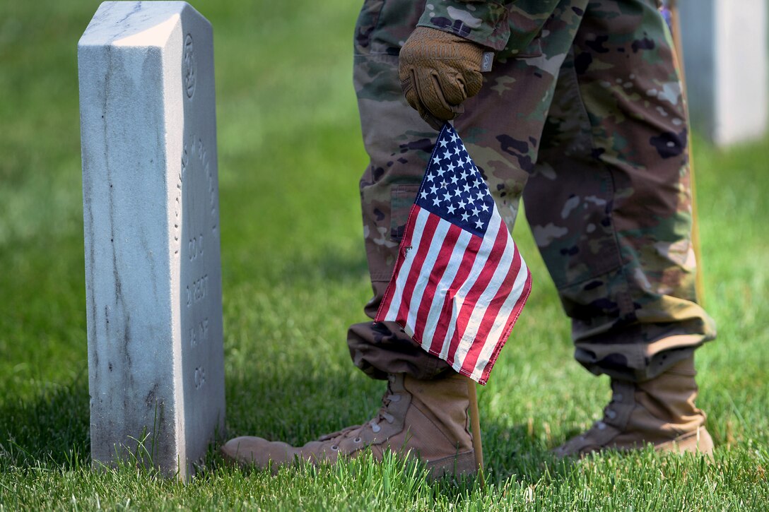 A soldier places an American flag in front of a headstone during "Flags In" at Arlington National Cemetery in Arlington, Va., May 26, 2016. DoD photo by Marvin D. Lynchard