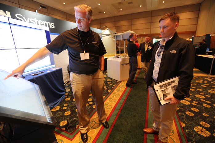 Ken Phillips,left, showcases an exhibit during the 45th Annual Marine Corps Aviation Association Symposium and Marine Aviation Summit at New Bern, N.C., May 17, 2016. Hundreds of naval aviators gathered at the convention center for the opening brief to the weeklong event. Senior leaders gathered to discuss the future of Marine Corps aviation and the steps the Corps is taking to reach its set goals. Phillips is a manager with Textron Systems. (U.S. Marine Corps photo by Cpl. N.W. Huertas/Released)