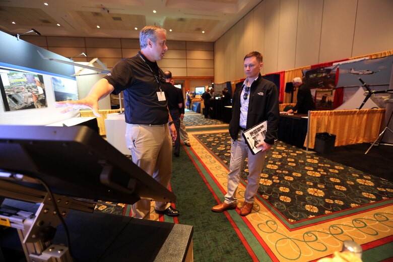 Ken Phillips,left, showcases an exhibit during the 45th Annual Marine Corps Aviation Association Symposium and Marine Aviation Summit at New Bern, N.C., May 17, 2016. Hundreds of naval aviators gathered at the convention center for the opening brief to the weeklong event. Senior leaders gathered to discuss the future of Marine Corps Aviation and the steps the Corps is taking to reach its set goals. Phillips is a manager with Textron Systems. (U.S. Marine Corps photo by Cpl. N.W. Huertas/Released)