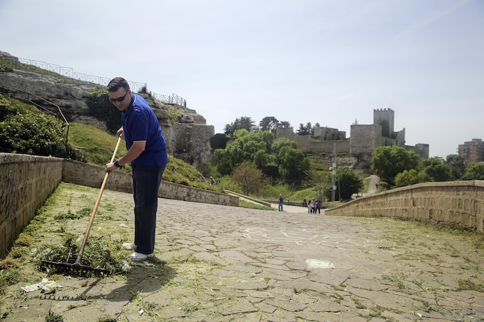 Lt. Arthur Briggs, the chaplain with Special Purpose Marine Air-Ground Task Force Crisis Response-Africa Logistics Combat Element, rakes up garbage and debris at Castello di Lombardia in Enna, Sicily, during a community relations project on April 22, 2016.  Marines assist local areas in various projects to build relationships with the Sicilian government and people.  (U.S. Marine Corps photo by Cpl. Alexander Mitchell/released)