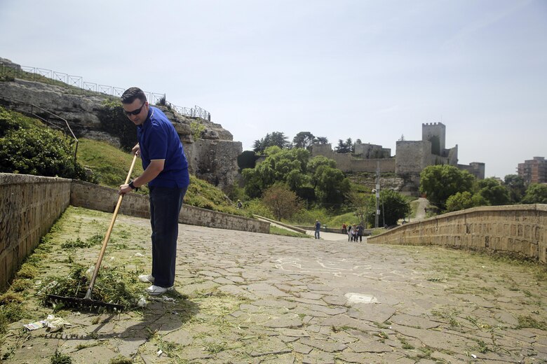 Lt. Arthur Briggs, the chaplain with Special Purpose Marine Air-Ground Task Force Crisis Response-Africa Logistics Combat Element, rakes up garbage and debris at Castello di Lombardia in Enna, Sicily, during a community relations project on April 22, 2016.  Marines assist local areas in various projects to build relationships with the Sicilian government and people.  (U.S. Marine Corps photo by Cpl. Alexander Mitchell/released)