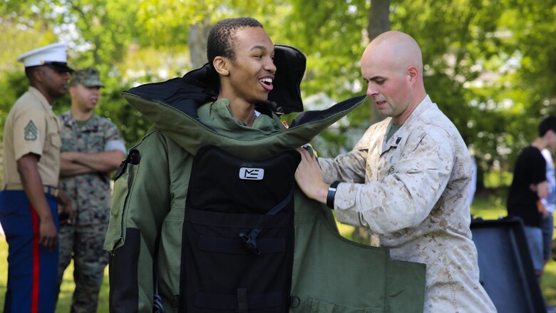 Staff Sgt. Adam Morris, an explosive ordnance disposal technician, helps a high school student try on an EOD bomb suit during a Marine Air Ground Task Force demonstration at Massapequa High School in Long Island, New York. The Marines are visiting the city to interact with the public, demonstrate capabilities and teach the people of New York about America's sea services.