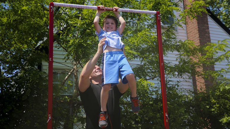 Sgt. Eli Rhodes, a recruiter with Recruiting Substation Hicksville in New York, helps a young child up on the pull up bar during a Marine Air Ground Task Force demonstration at Massapequa High School in Long Island, New York. The Marines are visiting the city to interact with the public, demonstrate capabilities and teach the people of New York about America's sea services.