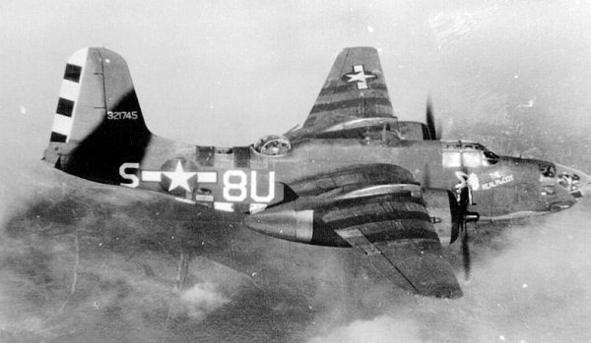 An A-20J Havoc attack bomber named “The Real McCoy” of Thad C. Williams’ 646th Bomb Squadron (Light, squadron code 8U) of the 410th Bomb Group (Light) is seen over a broken cloud deck late during World War II.  The A-20J featured am acrylic glass nose which allowed the aircraft to carry a bombardier and bombsight (seen in the photo) and serve as a formation leader in bombing missions, especially for the more numerous gun-nosed version of the Havoc bombers.  The serial number for this aircraft, 43-21745, is only a few numbers away from the A-20J that Thad Williams flew on his last combat mission, 43-21740.  This picture was taken some time after D-Day as the recognition stripes atop the aircraft have been painted out.  (USAF Photo)