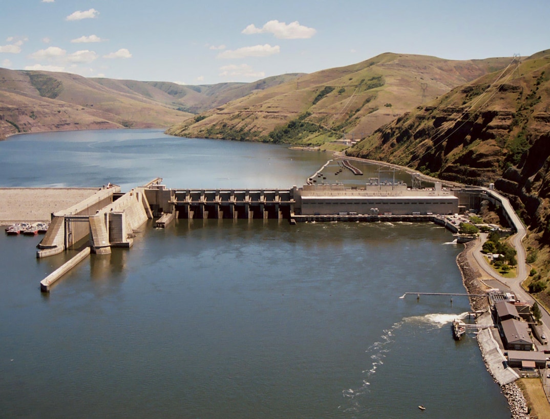 Lower Granite Lock and Dam on the Snake River and its Juvenile Fish Facility (JFF), lower right, in this historic photo. As part of the Lower Granite Juvenile Bypass System (JBS) improvements, a new elevated Juvenile Transportation Channel is being constructed between the JFF and the dam, above the roadway, parking lots and adult fish ladder on the right (new construction is not seen in this historic photo). The new elevated channel will help juvenile fish migrate downstream. US Army Corps of Engineers photo.