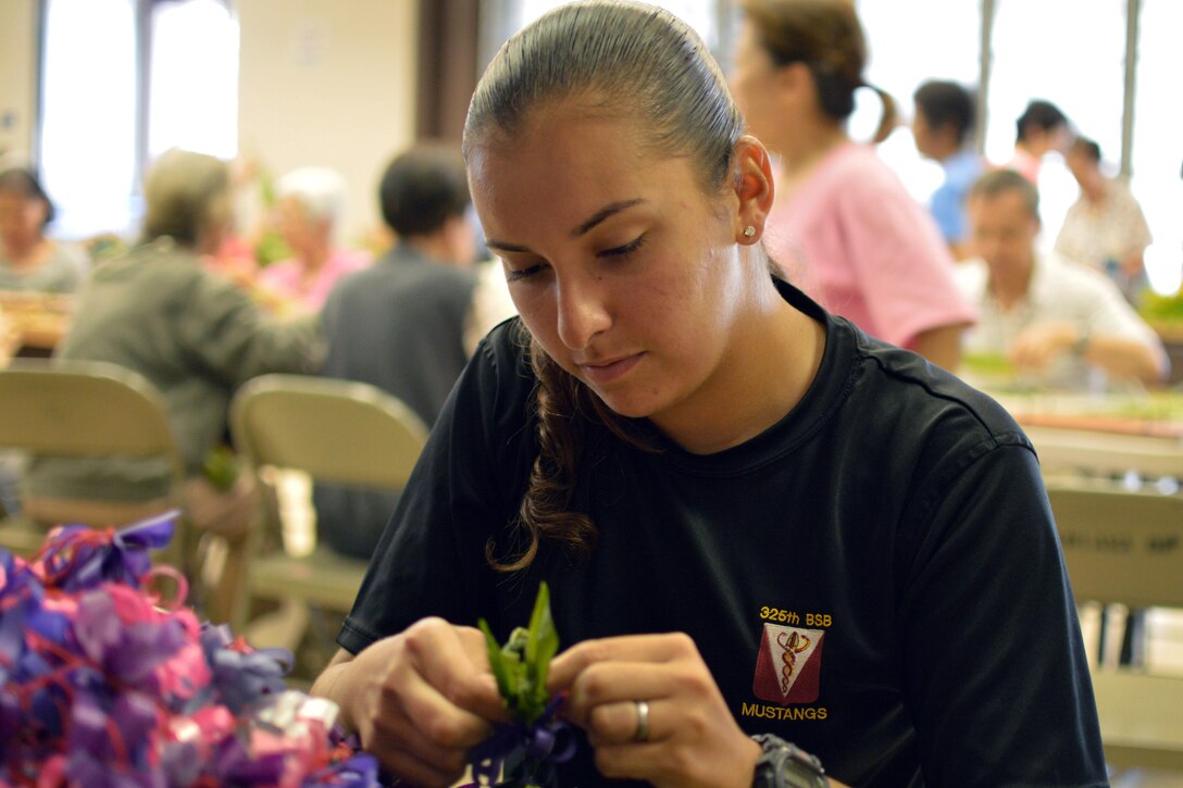 Army Pfc. Vanessa Sheika ties a bow around a lei at the Wahiawa District Park, Hawaii, May 27, 2016. Sheika was one of several soldiers to work with the Wahiawa Rainbow Seniors to produce nearly 2,300 leis for headstones at the Schofield Barracks Post Cemetery to mark Memorial Day. Sheika is assigned to the  25th Infantry Division's 325th Brigade Support Battalion, 3rd Brigade Combat Team. Army photo by Staff Sgt. Armando R Limon