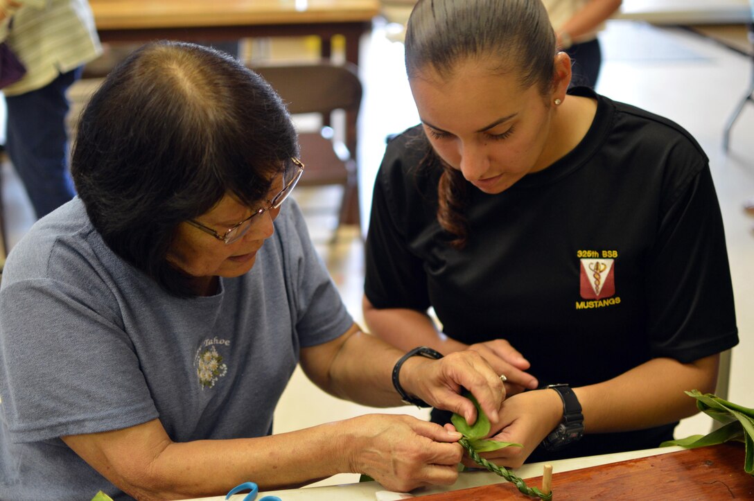 Linda Hirano, a Wahiawa Rainbow Seniors volunteer, shows Army Pfc. Vanessa Sheika how to make a lei from a ti leaf in Honolulu, May 27, 2016. The senior citizens group and soldiers assigned to the 25th Infantry Division’s 3rd Brigade Combat Team made nearly 1,900 leis to place on headstones at the Schofield Barracks post cemetery for Memorial Day. Army photo by Staff Sgt. Armando R Limon