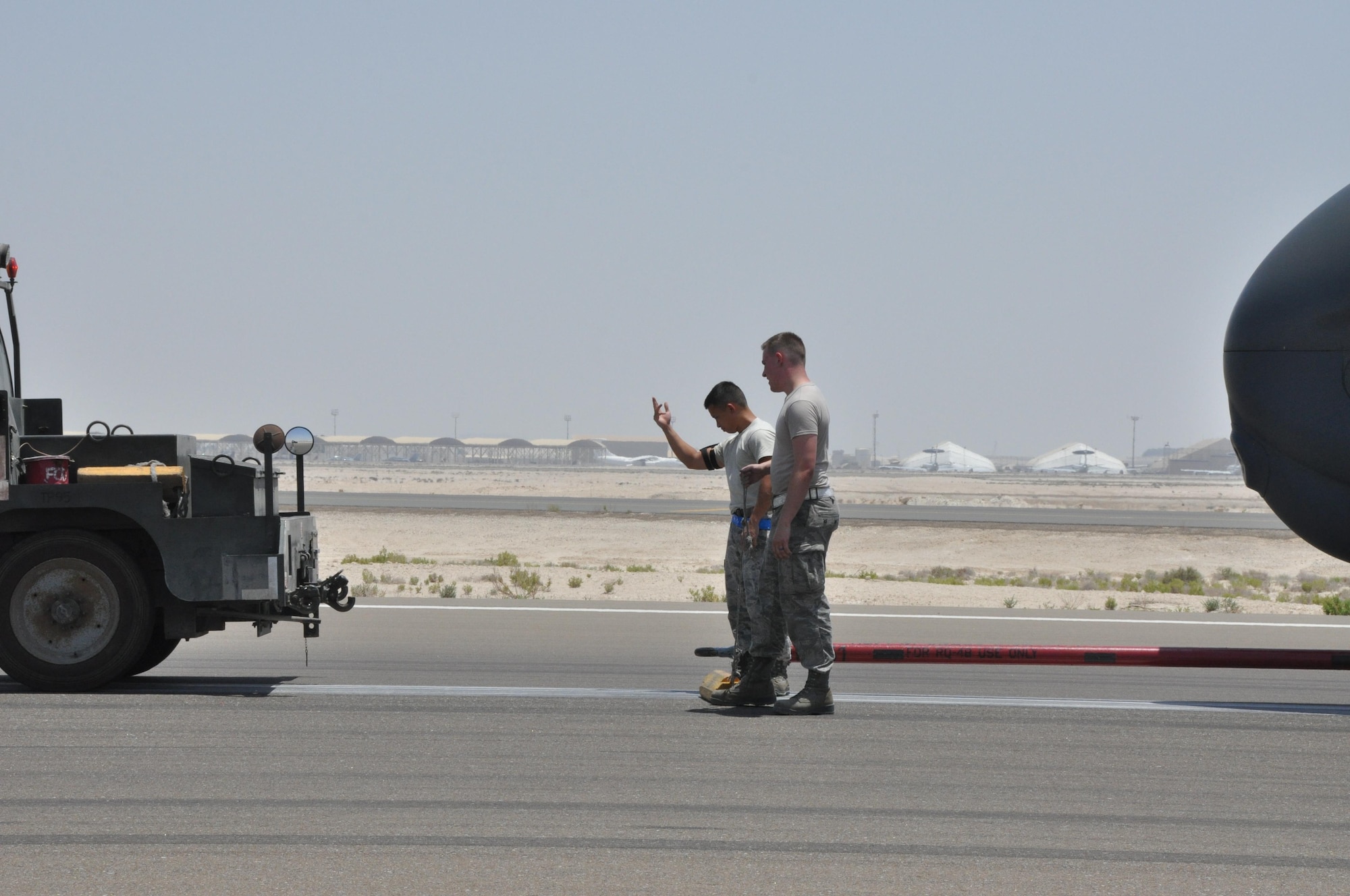 Staff Sgt. Phillip (left) and Senior Airman Alan (right), 380th Expeditionary Aircraft Maintenance Squadron Global Hawk technicians, spot a reversing vehicle to connect a tow bar to a RQ-4 Global Hawk, May 16. The Global Hawk is capable of providing near real-time information to assist in saving lives during worldwide peacetime, contingency and wartime operations. (U.S. Air Force photo by Staff Sgt. Samantha Mathison)