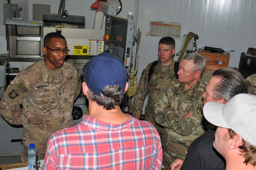 Staff Sgt. Robert Marshall (left), a machinist with 1109th Theatre Aviation Sustainment Maintenance Group, talks to Matthew Lillard (blue hat), Gen. Frank Grass (center), the chief of the National Guard Bureau, Robert Patrick (black shirt) and Jerrod Neimann (white hat) about helicopter parts he created on Camp Arifjan, Kuwait, May 18, 2016. This visit was part of the USO May Madness Tour.