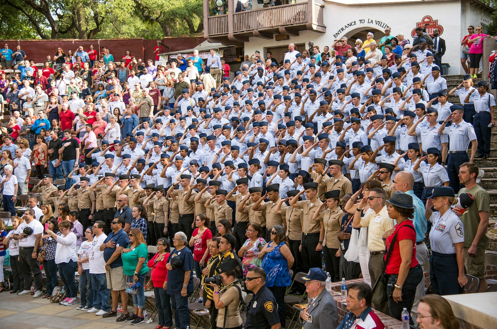 Airmen and Sailors from Joint Base San Antonio salute as members of San Antonio held their hands over their heart as the National Anthem is played by during the Armed Forces River Parade May 21 at the San Antonio Riverwalk. The parade is an annual event held in San Antonio to honor service members past and present.