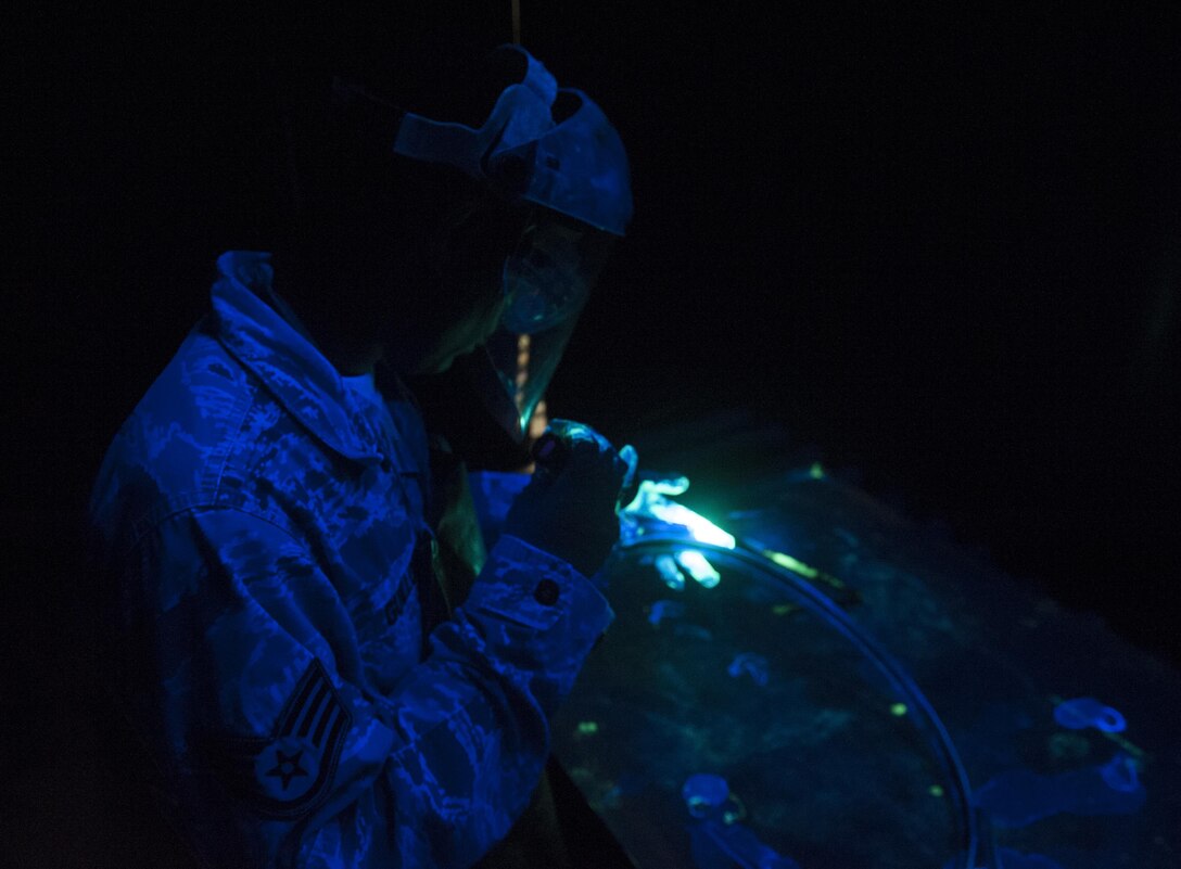 U.S. Air Force Staff Sgt. Nicholas Guillory, 489th Maintenance Squadron nondestructive inspection craftsman, inspects a C-130J Super Hercules tailpipe clamp at Dyess Air Force Base, Texas, Oct. 24, 2016. After treating the component with a penetrant solution, any cracks unseen by the naked eye glow under ultraviolet light. (U.S. Air Force photo by Airman 1st Class Rebecca Van Syoc)