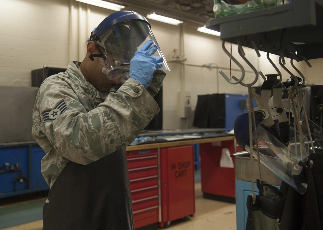 U.S. Air Force Staff Sgt. Nicholas Guillory, 489th Maintenance Squadron nondestructive inspection craftsman, dons his personal protective equipment before starting parts inspection at Dyess Air Force Base, Texas, Oct. 24, 2016. When working with chemicals in some techniques of inspection, Airmen must wear gloves, aprons, goggles and face shields to keep them safe. (U.S. Air Force photo by Airman 1st Class Rebecca Van Syoc)