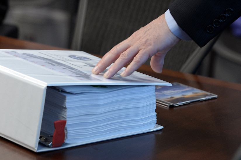 A hand rests on a display symbolizing how massive binders of financial tracking information paper trails have been pared down to software that can fit onto a single compact disc during a briefing at the Pentagon about F-35 cost tracking software developed by the Defense Department and contractor Lockheed Martin, Nov. 1, 2016. DoD photo by EJ Hersom