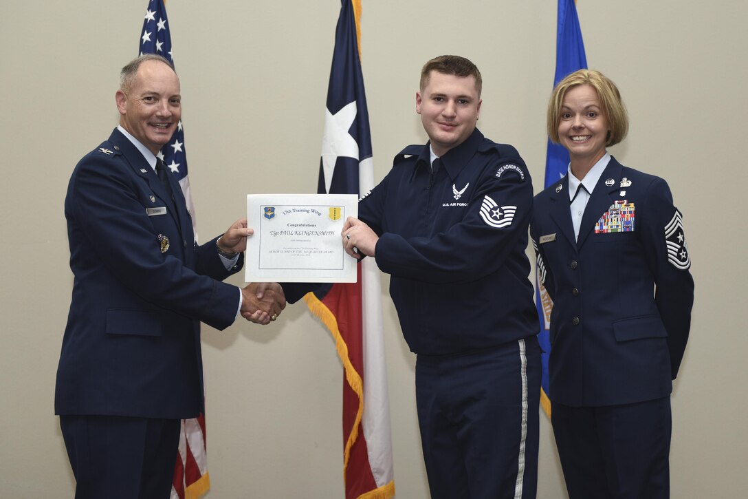 U.S. Air Force Col. Michael Downs, 17th Training Wing Commander, and Chief Master Sgt. Bobbie Riensche, 17th TRW Command Chief, present the Honor Guard Member of the Quarter to Tech. Sgt. Paul Klingensmith, 316th Training Squadron, during the wing quarterly awards ceremony at the Event Center on Goodfellow Air Force Base, Texas, Oct. 31, 2016. (U.S. Air Force photo by Airman 1st Class Chase Sousa/Released)