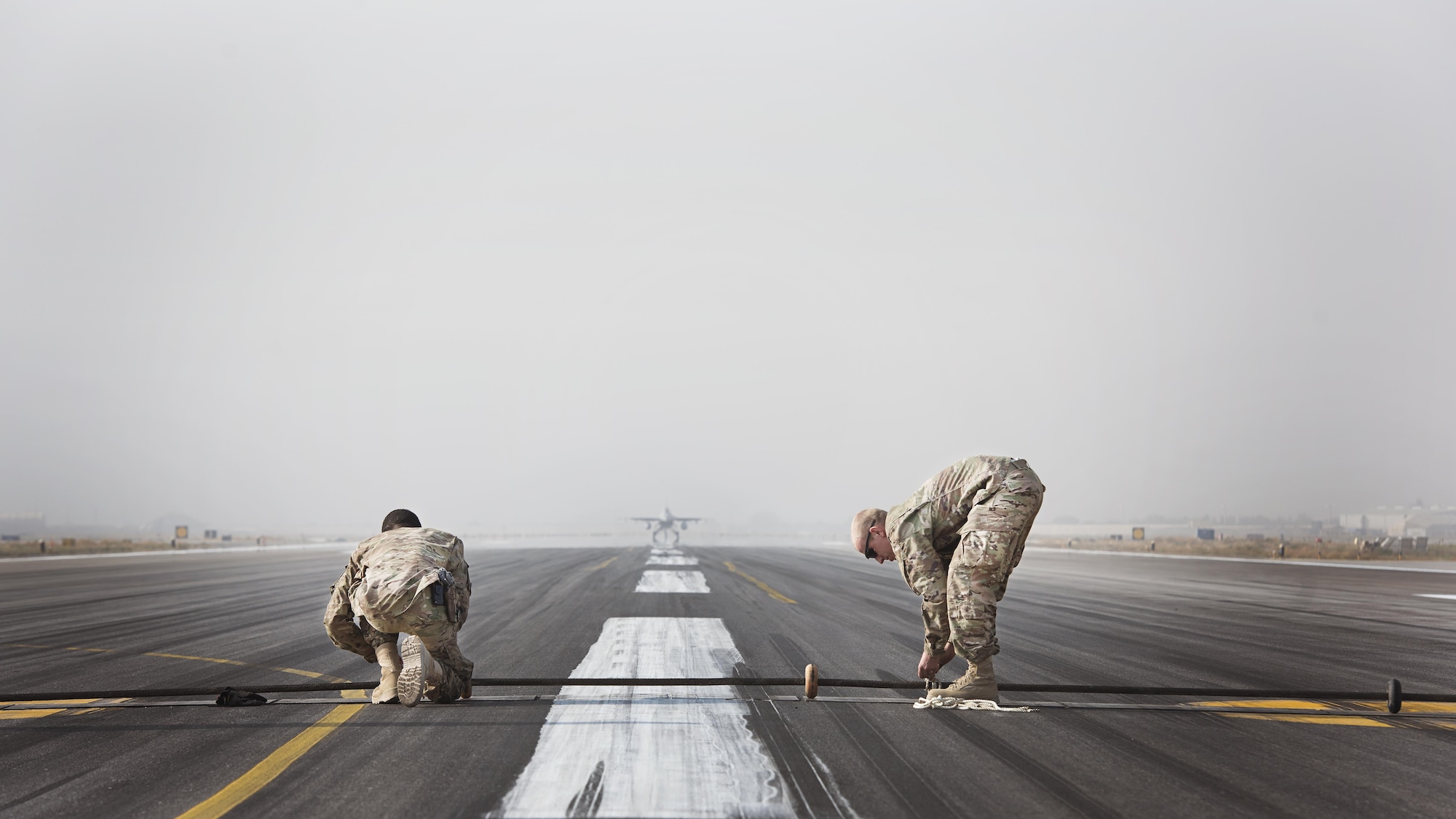 Senior Airmen Mathew Chapman and Devin Tillman, 455th Expeditionary Civil Engineer Squadron power production specialists, place a Mobile Aircraft Arresting System cable across the runway at Bagram Airfield Afghanistan, during a certification test Oct. 30, 2016. The MAAS is a barrier used to catch the arresting hook on fighter aircraft in case of malfunction upon landing or take off. (U.S. Air Force photo by Staff Sgt. Katherine Spessa)