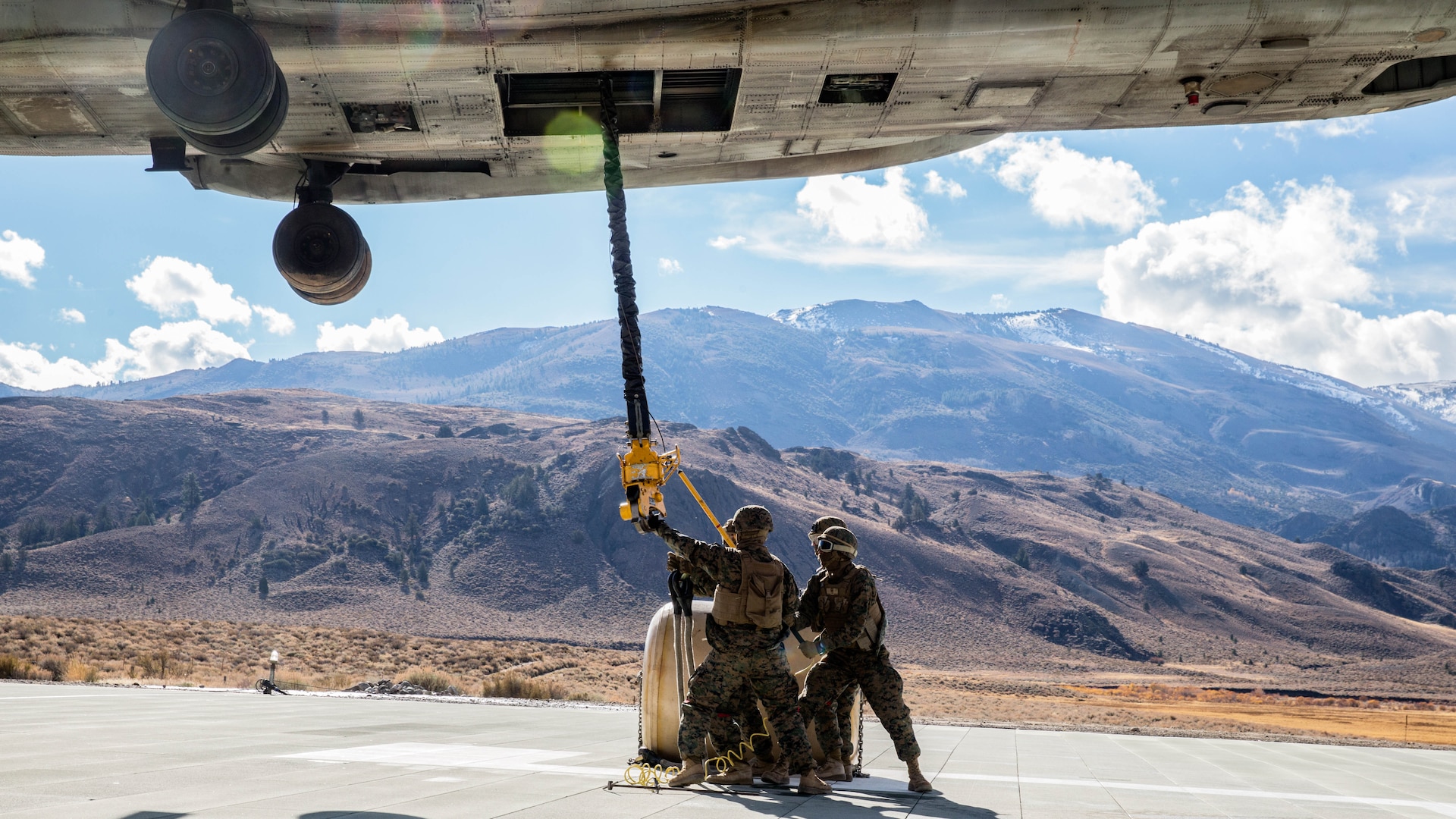 U.S. Marines with Combat Logistics Battalion 15, 1st Marine Logistics Group, and 3rd Battalion, 4th Marine Regiment, 1st Marine Division, grab a hook lowered by a CH-53E Super Stallion, with Marine Heavy Helicopter Squadron 466, to pick up a 500-gallon drum of water during a Helicopter Support Team drill at Mountain Warfare Training Center, Bridgeport, California, Oct. 25, 2016. The Marines use a pole to grab the hook lowered by the helicopter to ground the electrical currents before grabbing it by hand. The drum was taken into the Sierra Mesa Mountains to support Marines who are conducting field operations during Mountain Exercise 6-16. 