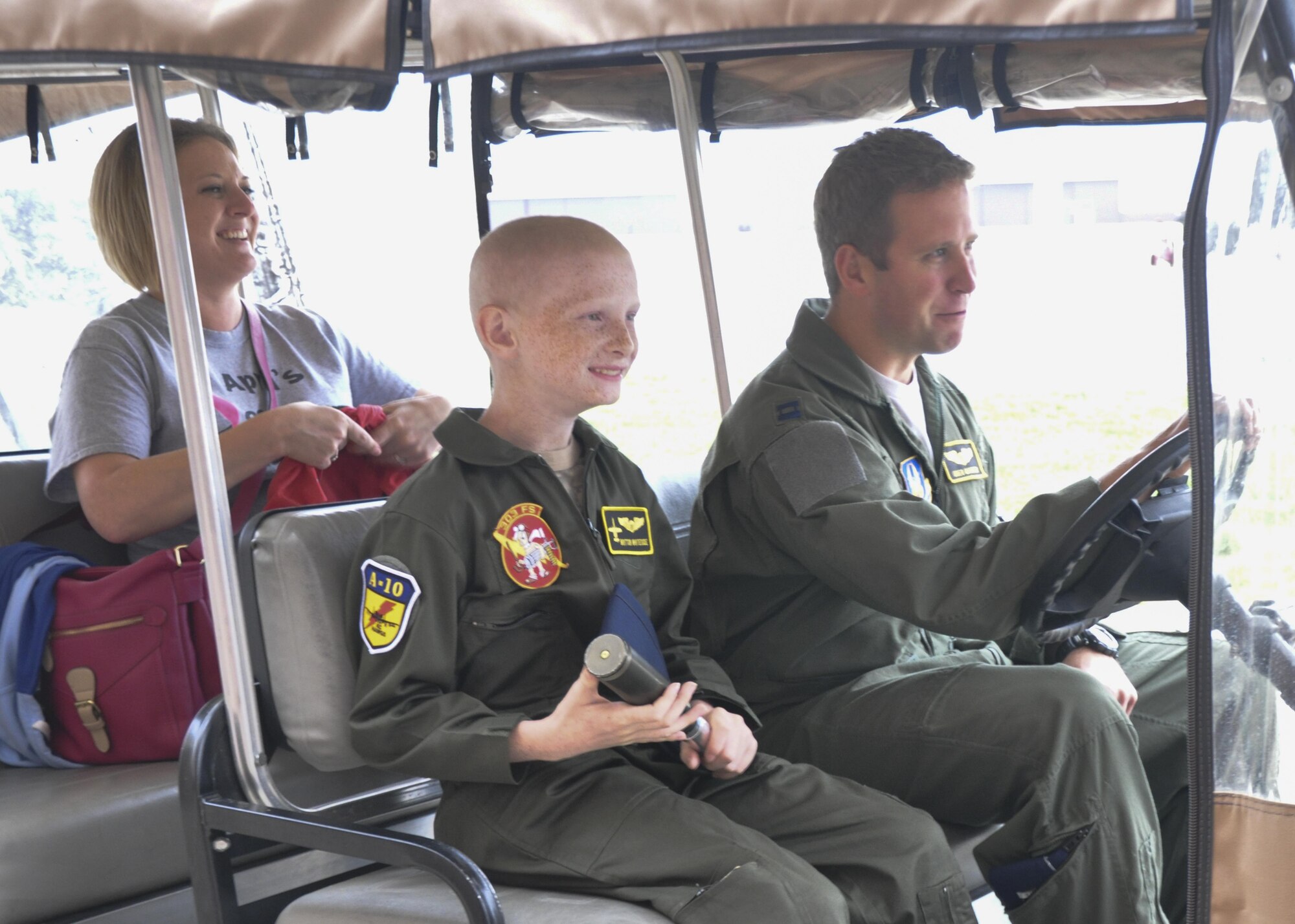 U.S. Air Force Capt. Geoffrey Manter, 303rd Fighter Squadron pilot, prepares to "race" another pilot in a golf cart to the squadron headquarters building at Whiteman Air Force Base as Britton Whiteside, honorary "pilot of the day," and his mom laugh. Britton and his parents were given a presentation of aircrew flight equipment then experienced a simulated flight. His family coordinated a visit at Whiteman before his final round of chemotherapy. (U.S. Air Force photo/Senior Airman Missy Sterling)