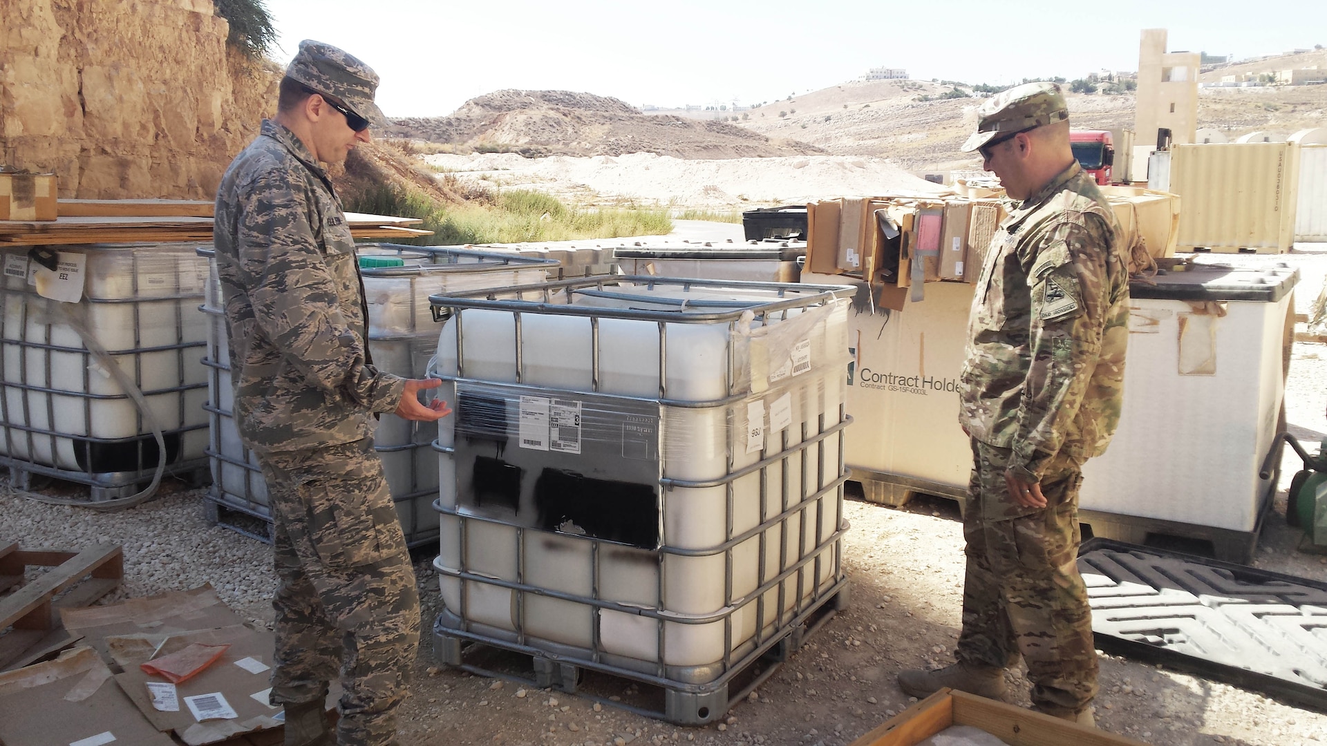An Army and an Air Force engineer review a pallet of containers of DLA-provided ground-hardening paste, commonly called “rhino snot,” which is used to reduce dust. This shipment was used to coat a makeshift runway for an unmanned aerial system.