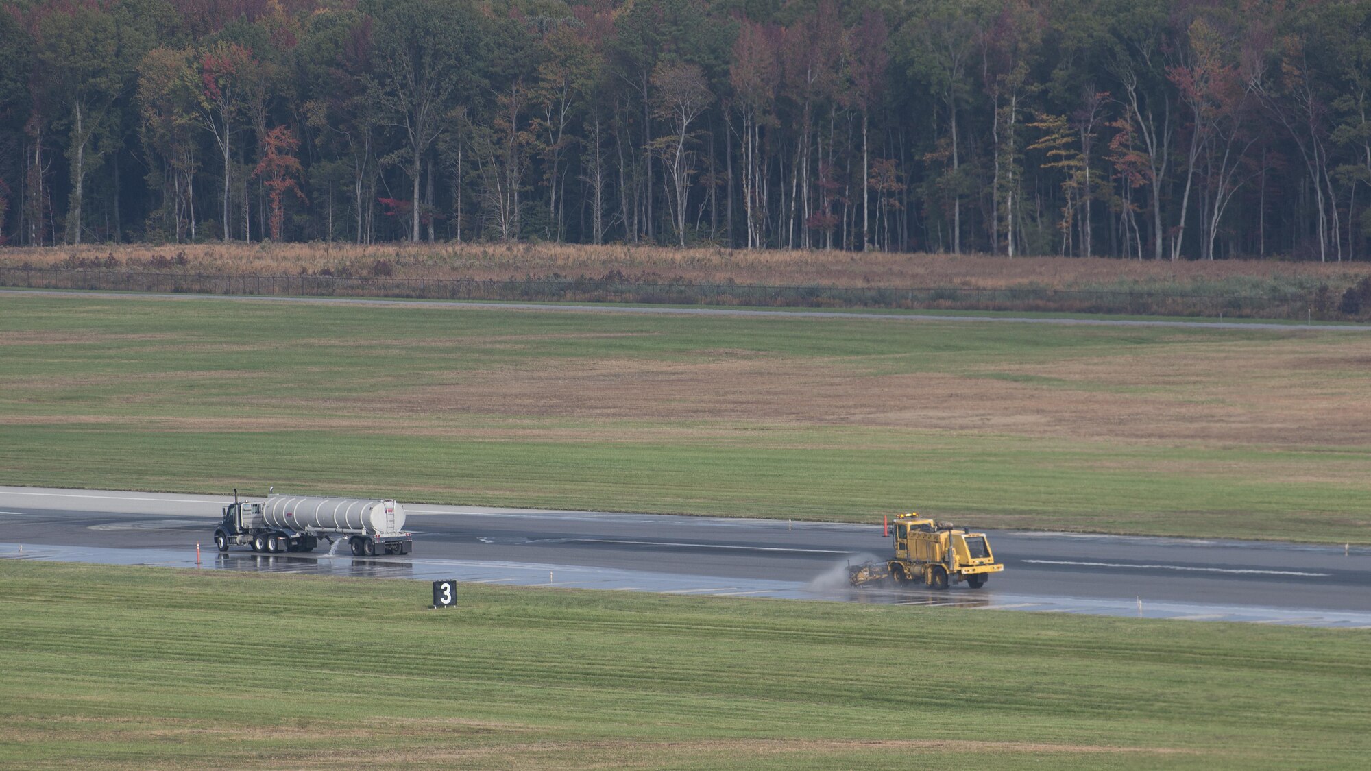 A water tanker truck disperses water as an Oshkosh Snow Broom brushes rubber residue off of Runway 14-32 during rubber removal operations Nov. 1, 2016, at Dover Air Force Base, Del. Rubber removal operations occur every six months in accordance with the amount of air traffic Dover AFB handles. (U.S. Air Force photo by Senior Airman Zachary Cacicia)