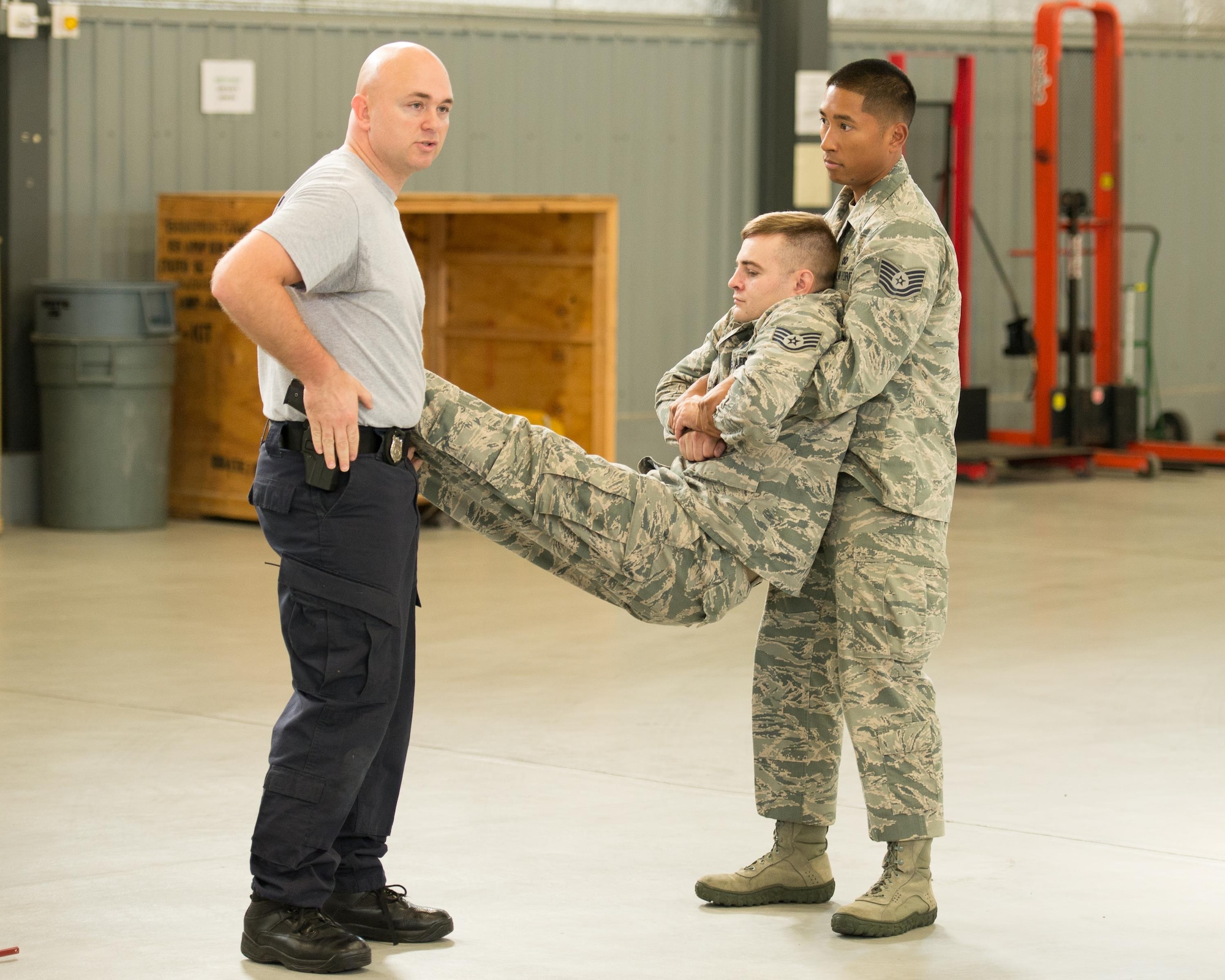 Senior Cpl. Jason Baxley, Delaware State Police Tactical Control Unit defensive tactics instructor, demonstrates a two-person carry with 436th Security Forces Squadron members to safely transport a non-compliant protestor Nov. 3, 2016, on Dover Air Force Base, Del. Here, Baxley stresses the importance of maintaining access to a side arm should the situation escalate. (U.S. Air Force photo by Mauricio Campino)