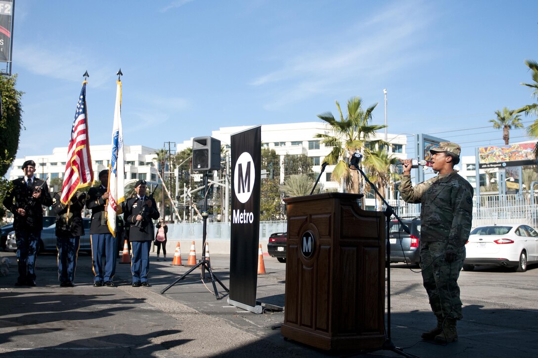 Sgt. Stephanie Jones, right, a cook with the 1916th Support Battalion stationed at Fort Irwin, Calif., sings the Star-Spangled Banner Nov. 4 while members of the 311th Expeditionary Sustainment Command, left, serve as a color guard for the unveiling of a plaque dedicated to Pvt. Joe Gandara. Gandara, killed in action in WWII, was awarded the Medal of Honor in 2014 as part of the Valor 24 program. (U.S. Army photo by Sgt. 1st Class Alexandra Hays, 79th Sustainment Support Command).