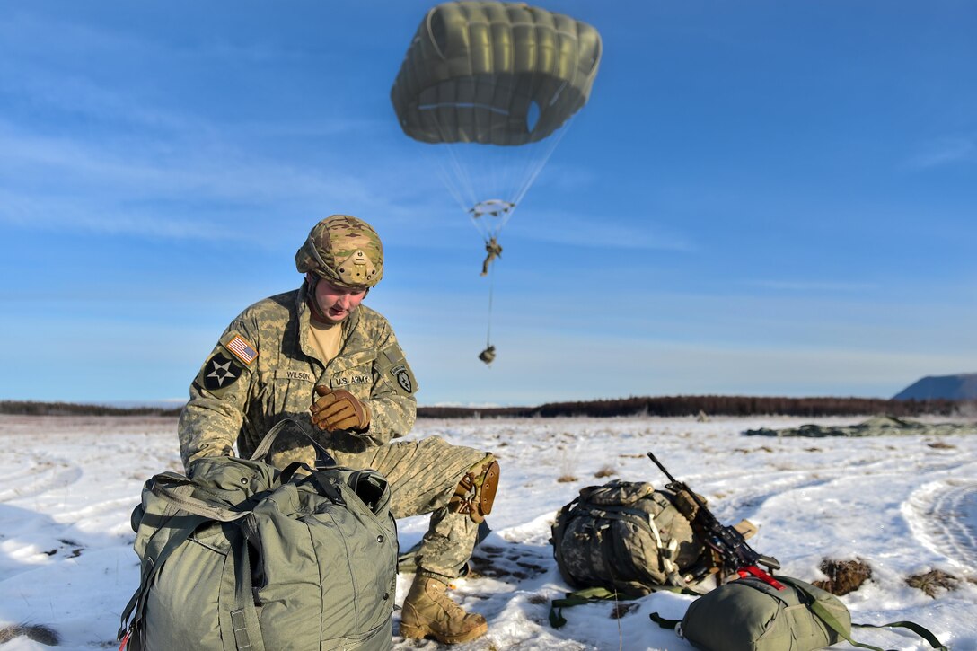 A paratrooper prepares to land while Army Sgt. Andrew Wilson, foreground, recovers his chute and equipment after an airborne training jump onto Malemute drop zone at Joint Base Elmendorf-Richardson, Alaska, Nov. 3, 2016. Wilson is assigned to the 25th Infantry Division’s 4th Infantry Brigade Combat Team (Airborne), Alaska. Air Force photo by Justin Connaher