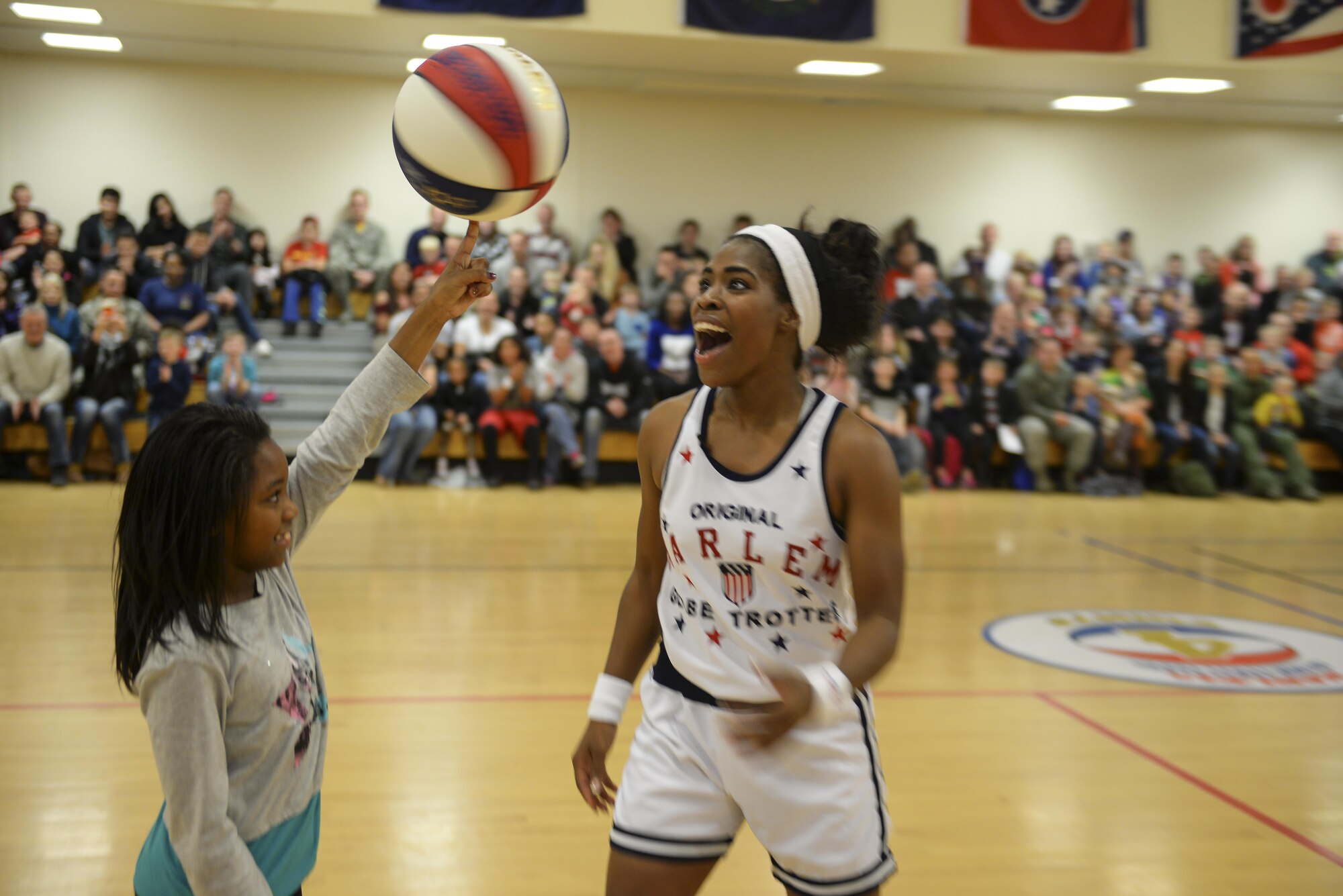 Harlem Globetrotters guard, TNT, watches a volunteer spin a basketball on her finger Nov. 4, 2016, at the Hardstand Fitness Center on RAF Mildenhall, England. Throughout the performance, audience members were selected to participate in the show. (U.S. Air Force photo by Staff Sgt. Micaiah Anthony)