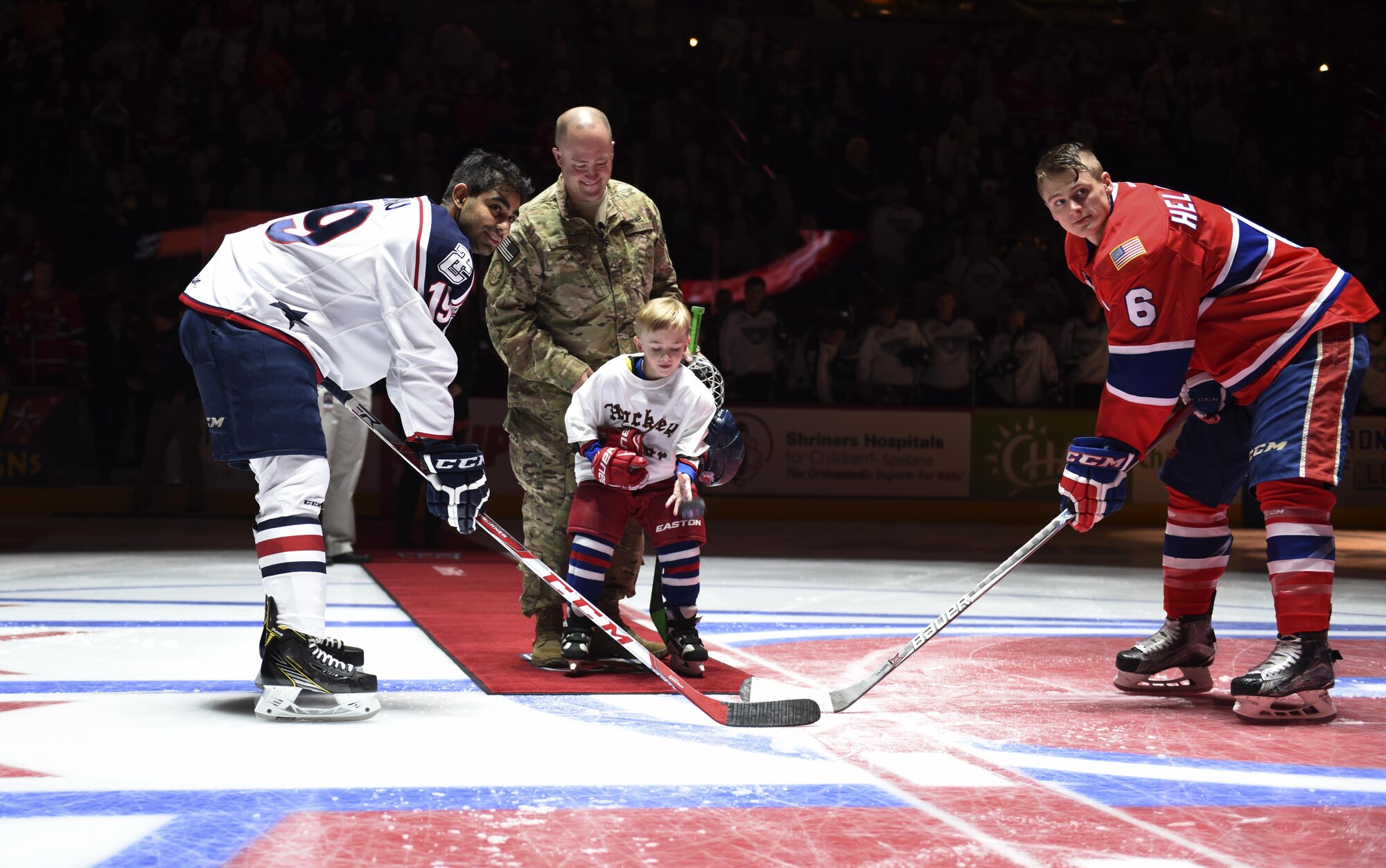 Master Sgt. Walter Weber, 92nd Security Forces Squadron flight sergeant, and his son perform the ceremonial puck drop during Military Appreciation Night Nov. 5, 2016, Spokane, Wash. The ceremonial first puck is a ritual of ice hockey in which the guest of honor drops a puck to mark the start of the game. (U.S. Air Force photo/Airman 1st Class Sean Campbell)