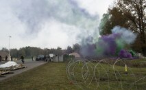 Green and purple smoke fills the sky as Airmen assigned to the 1st Combat Communications Squadron defend a base during a simulated attack during exercise Healthy Thunder at Ramstein Air Base, Germany, Nov. 4, 2016. In order to make the field training exercise portion of Healthy Thunder as real-world as possible, the Airmen used smoke grenades, ground burst simulators and blank rounds. (U.S. Air Force photo by Senior Airman Tryphena Mayhugh)