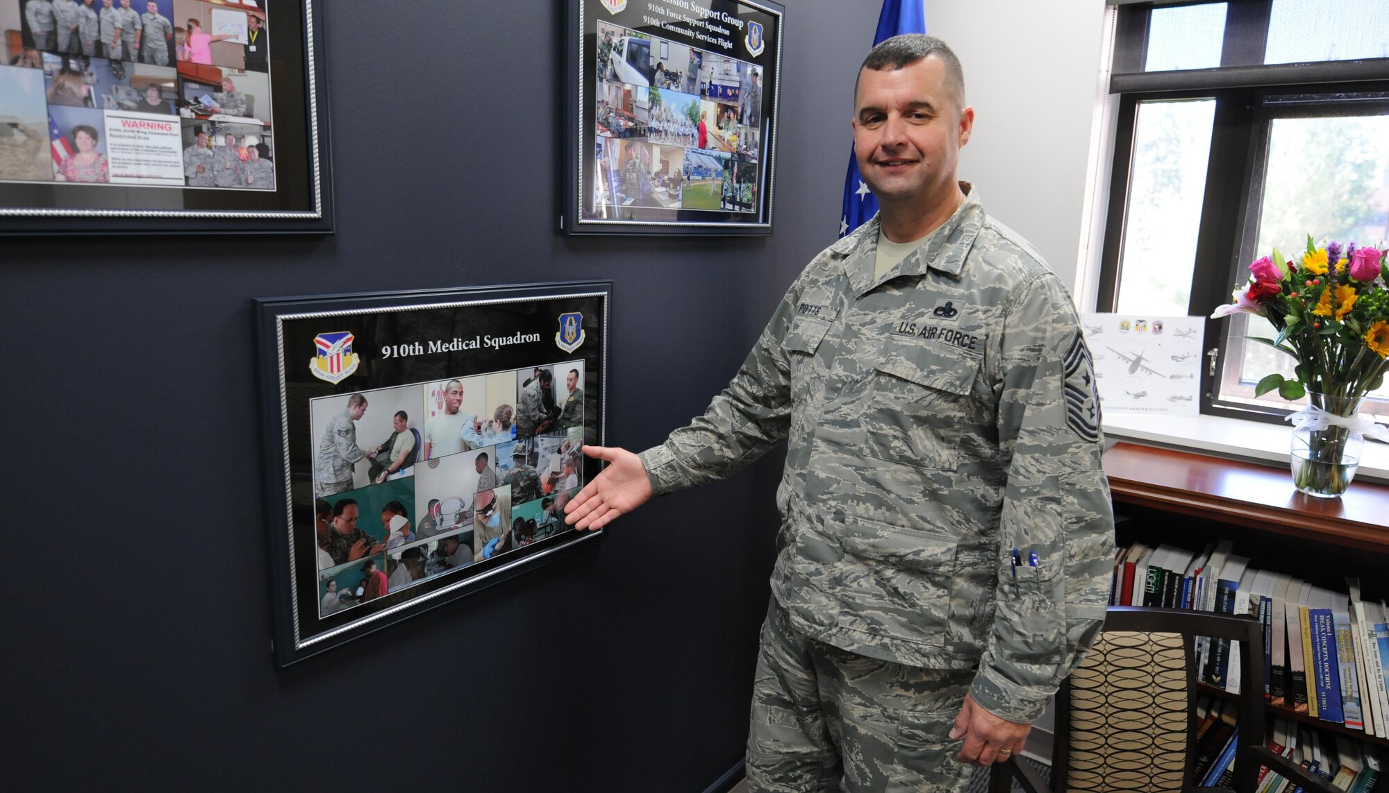 Air Force Reserve 910th Airlift Wing Command Chief Master Sgt. Robert Potts shows off one of the squadron photo collages hanging in the new wing’s Airman’s Suite during grand opening festivities for the space at the installation headquarters building here, November 6, 2016. The new facility highlights the accomplishments of base Units and serves a variety of purposes from meetings to promotion and awards boards. (U.S. Air Force photo/Tech. Sgt. James Brock)