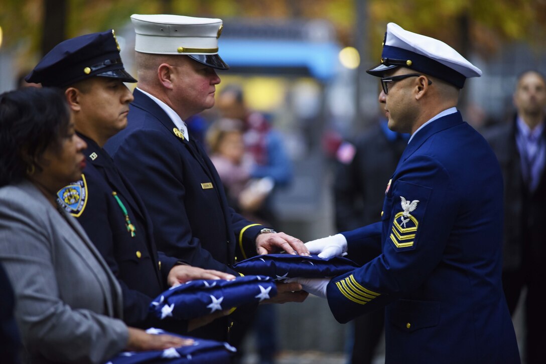 Army veteran Joseph Duggan Jr., a New York Fire Department battalion chief, accepts an American flag during a ceremony honoring the official grand marshals for the 2016 New York City Veterans Day Parade at the Freedom Tower in  New York City, Nov. 9, 2016. Duggan Jr., is a 9/11 first responder who served in Iraq as an Army Reserve captain. Coast Guard photo by Petty Officer 3rd Class Frank Iannazzo-Simmons