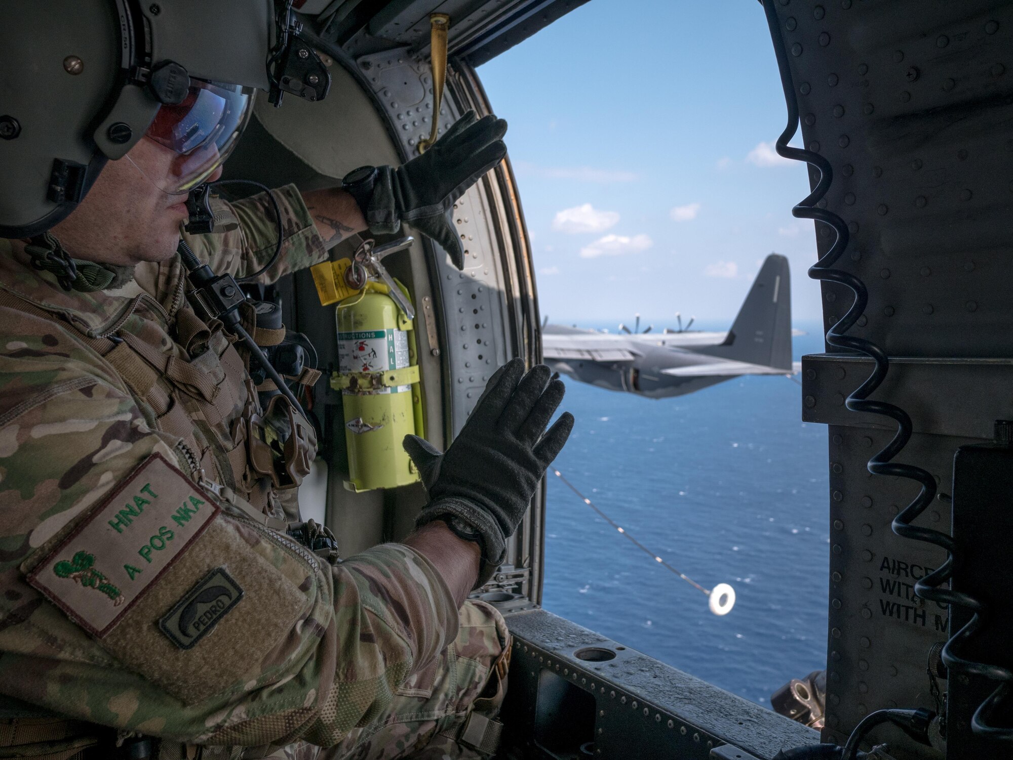 U.S. Air Force Master Sgt. Vincent Hnat, 33rd Rescue Squadron special mission aviator, communicates with aircrew on a MC-130J Commando II from the 17th Special Operations Squadron off the coast of Okinawa, Japan. During the training, members of the 33rd RQS performed an array of maneuvers and procedures to include helocasting, a simulated downed pilot in a hostile environment and helicopter air-to-air refueling. (U.S. Air Force photo by Senior Airman John Linzmeier)
