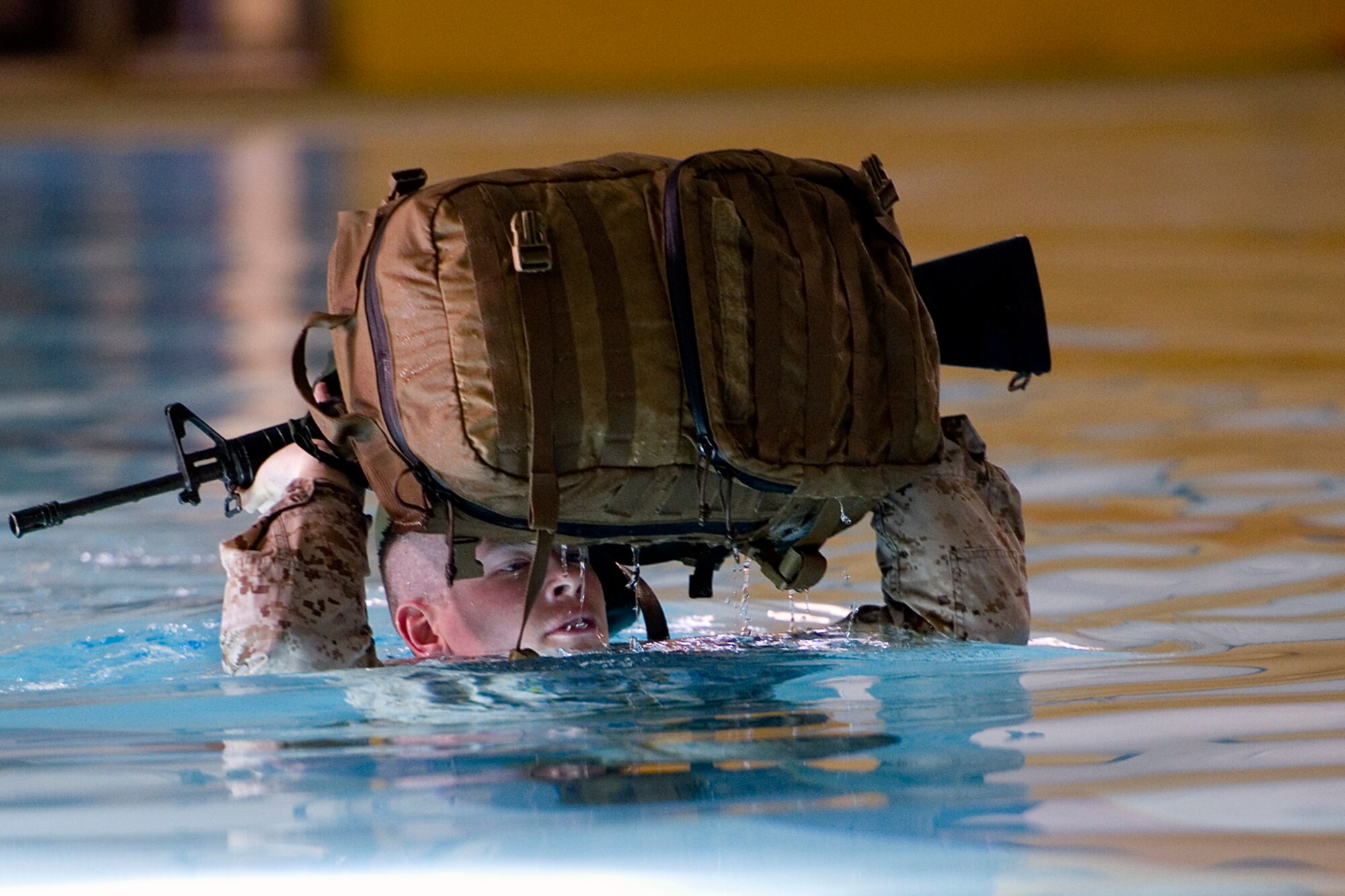 A Marine from Engineer Service Company, Combat Logistics Battalion, 254th Marine Logistics Group, holds his pack and rifle above his head during the 25-meter pack-swim portion of the Marine Corps water survival training program basic qualification at Great Lakes Naval Station, Ill., March 21, 2015. The program employs water survival skills designed to reduce fear, raise self-confidence, and develop Marines with the ability to survive in water. (U.S. Air Force photo/Tech. Sgt. Benjamin Mota)
